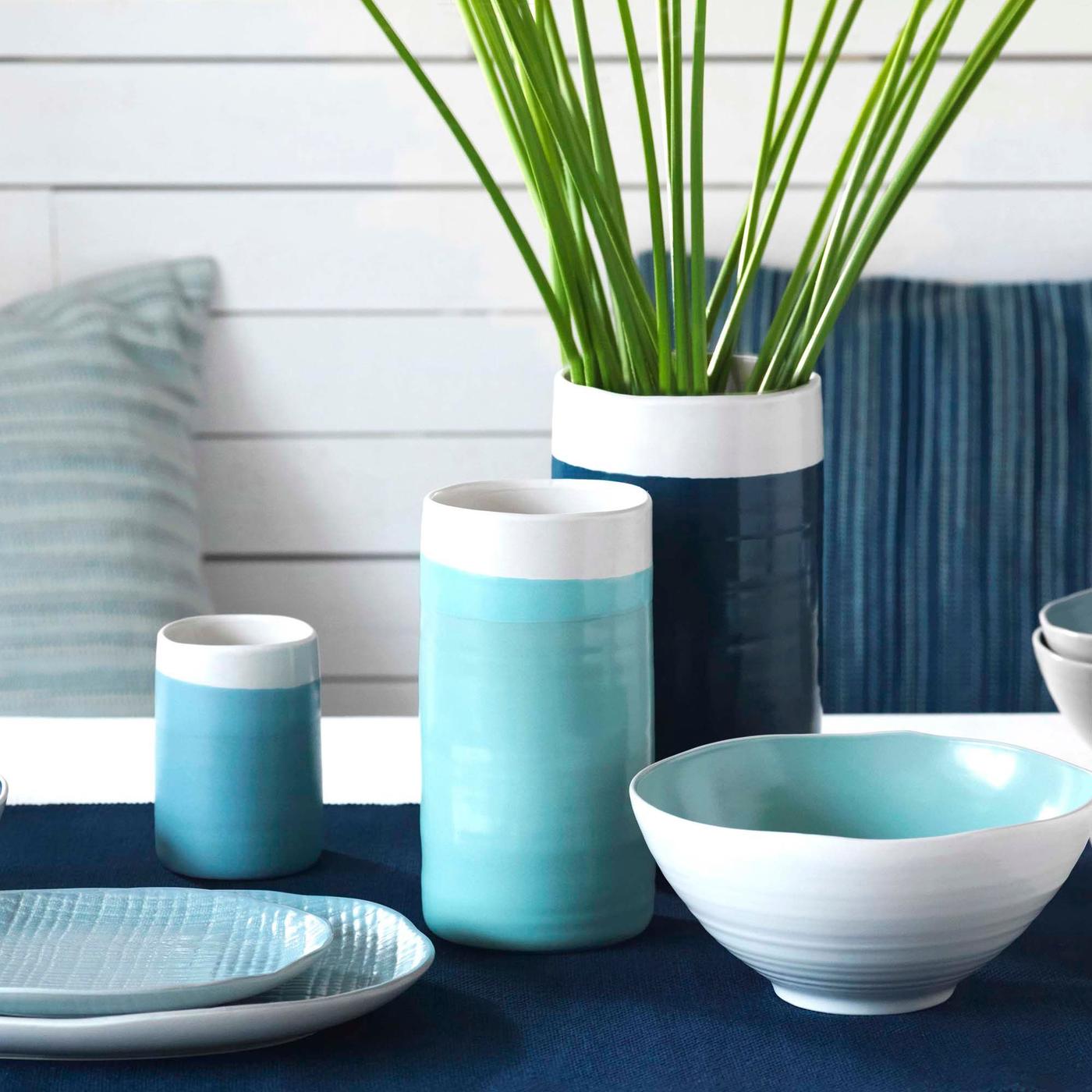 Three handmade, cylindrical ceramic BEDRIVA vases, plates and a bowl, all with glazes in different white and blue tonalities.