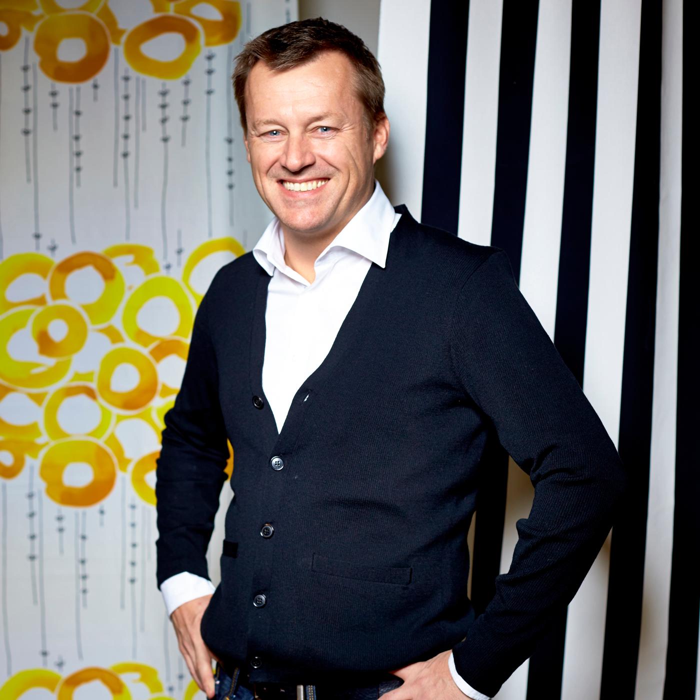 Jesper Brodin smiles at the camera. He stands with his hands on his hips against a stripe and print background.