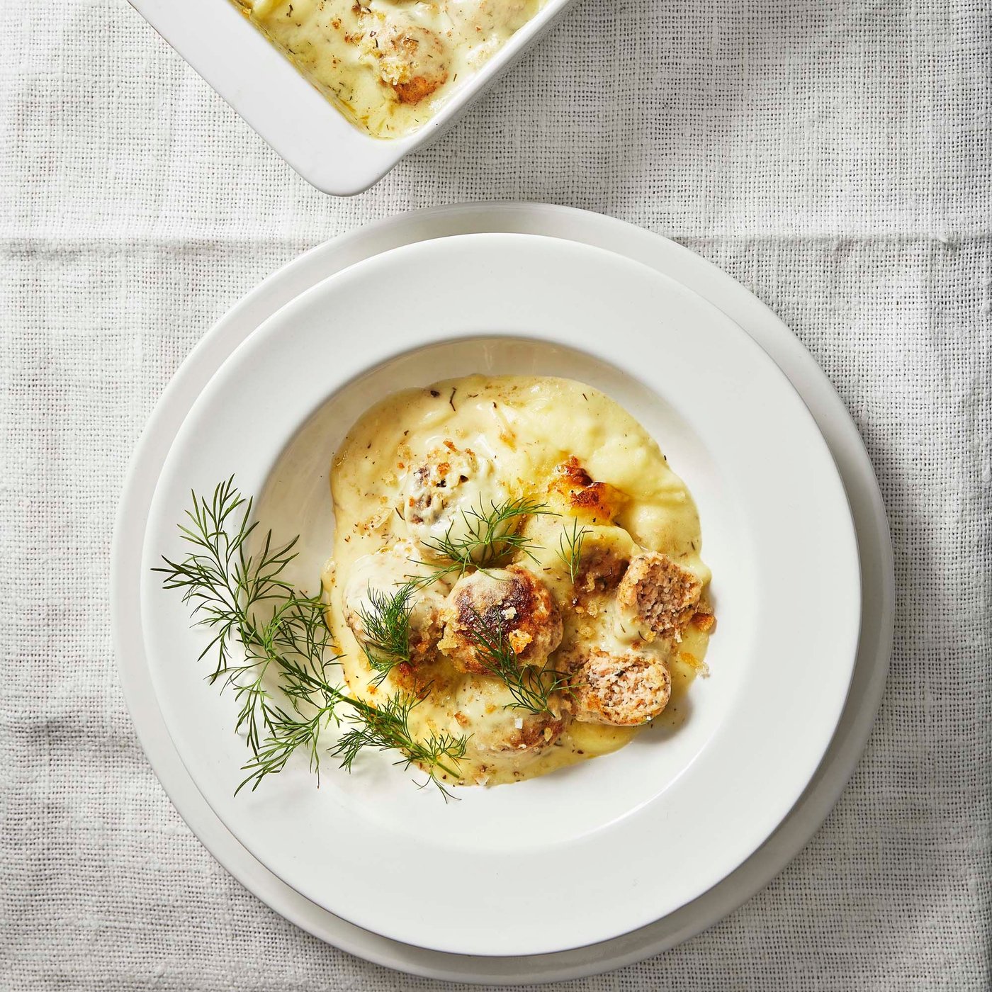 A white plate on a white tablecloth. The dish is IKEA salmon balls in a creamy sauce with a sprig of dill.