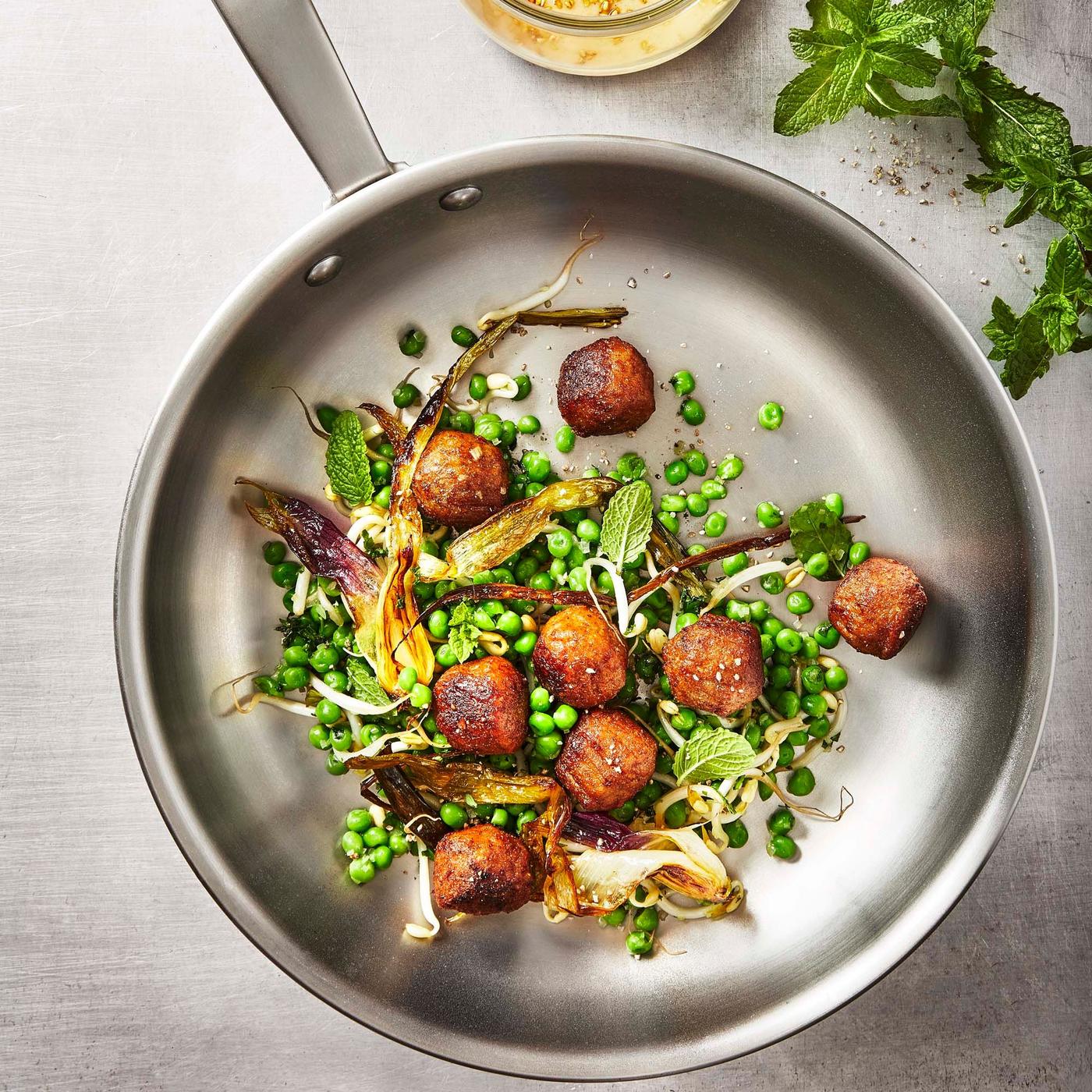 Huvudroll Plant balls in a metal frying pan, mixed with green peas, fennel and other vegetables. There are herbs nearby.