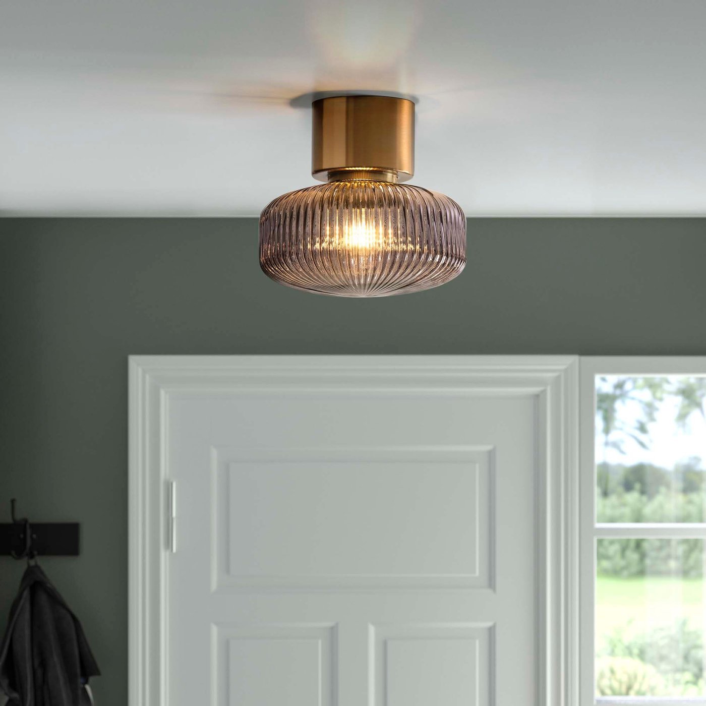 A decorative glass and brass flush mounted ceiling light in a green and white hallway.