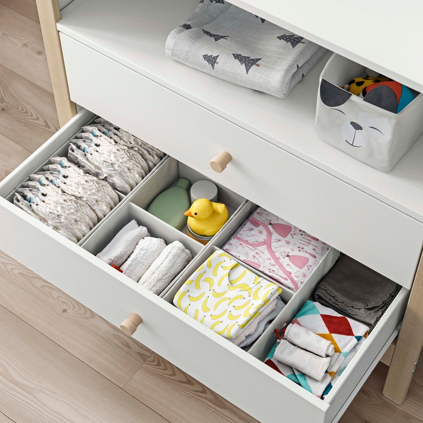 An open chest of drawers revealing neatly organised baby clothes.