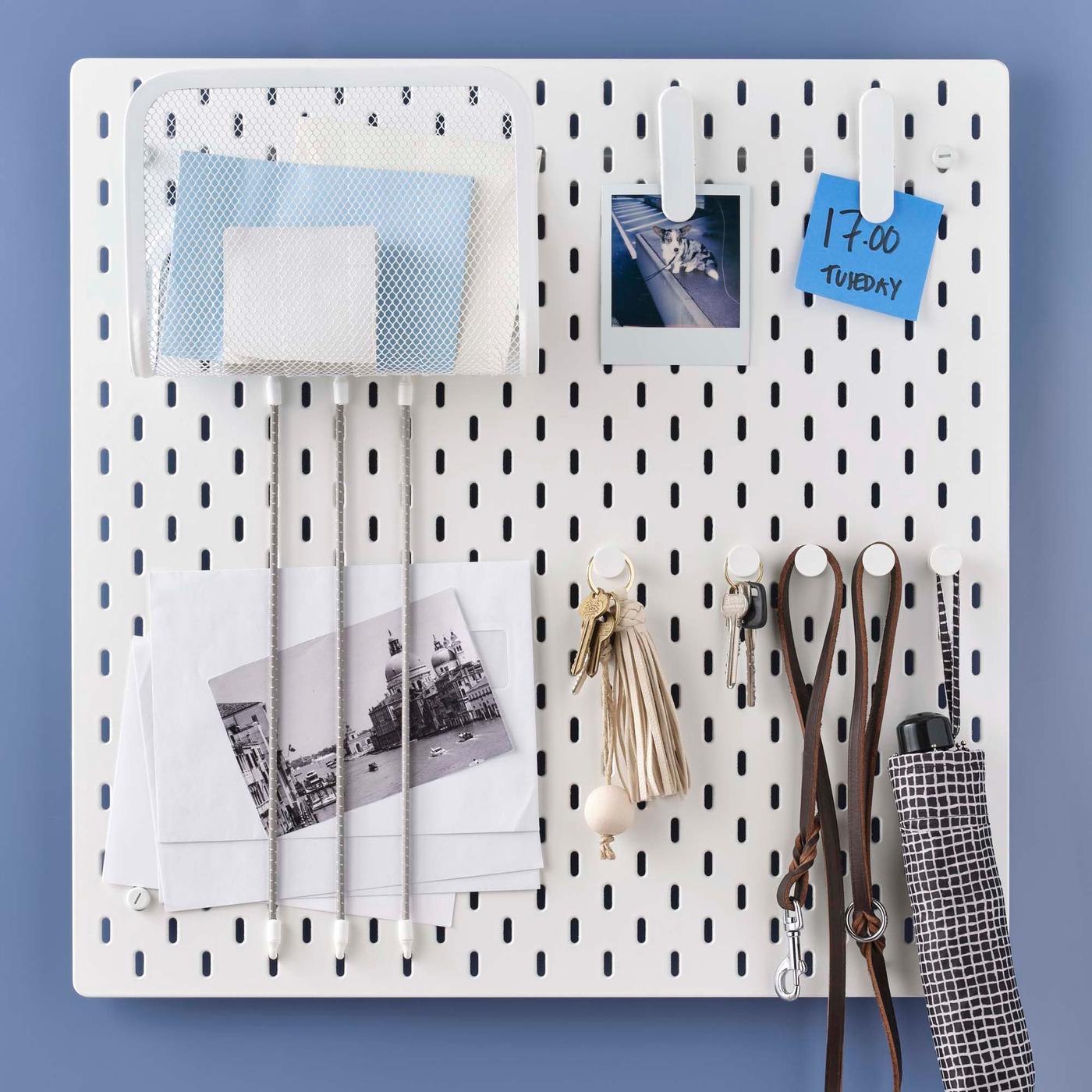 A white SKÅDIS pegboard with objects hanging and notes clipped on it.