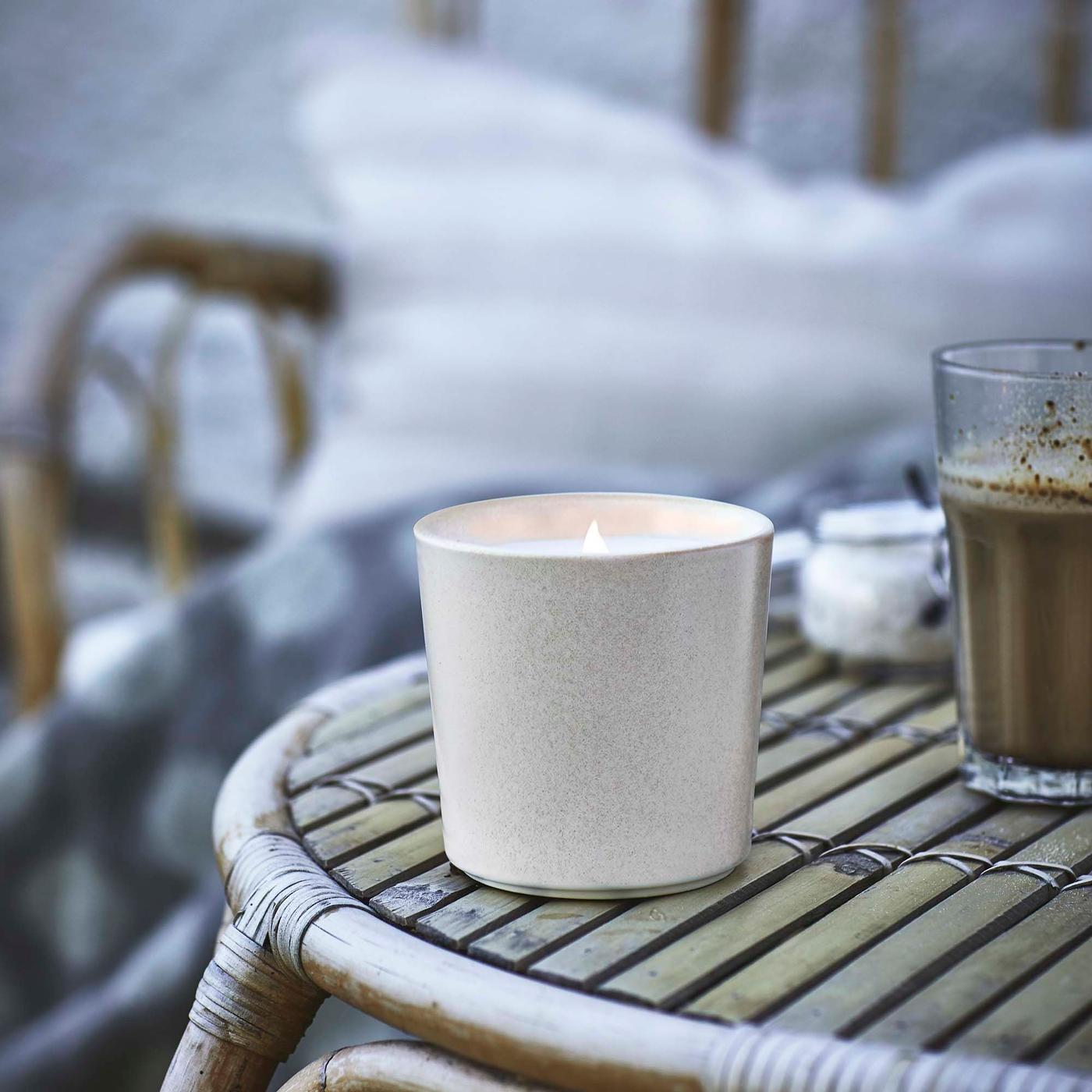 An illuminated candle on a bamboo table, with a cushion and blanket create a cosy look.