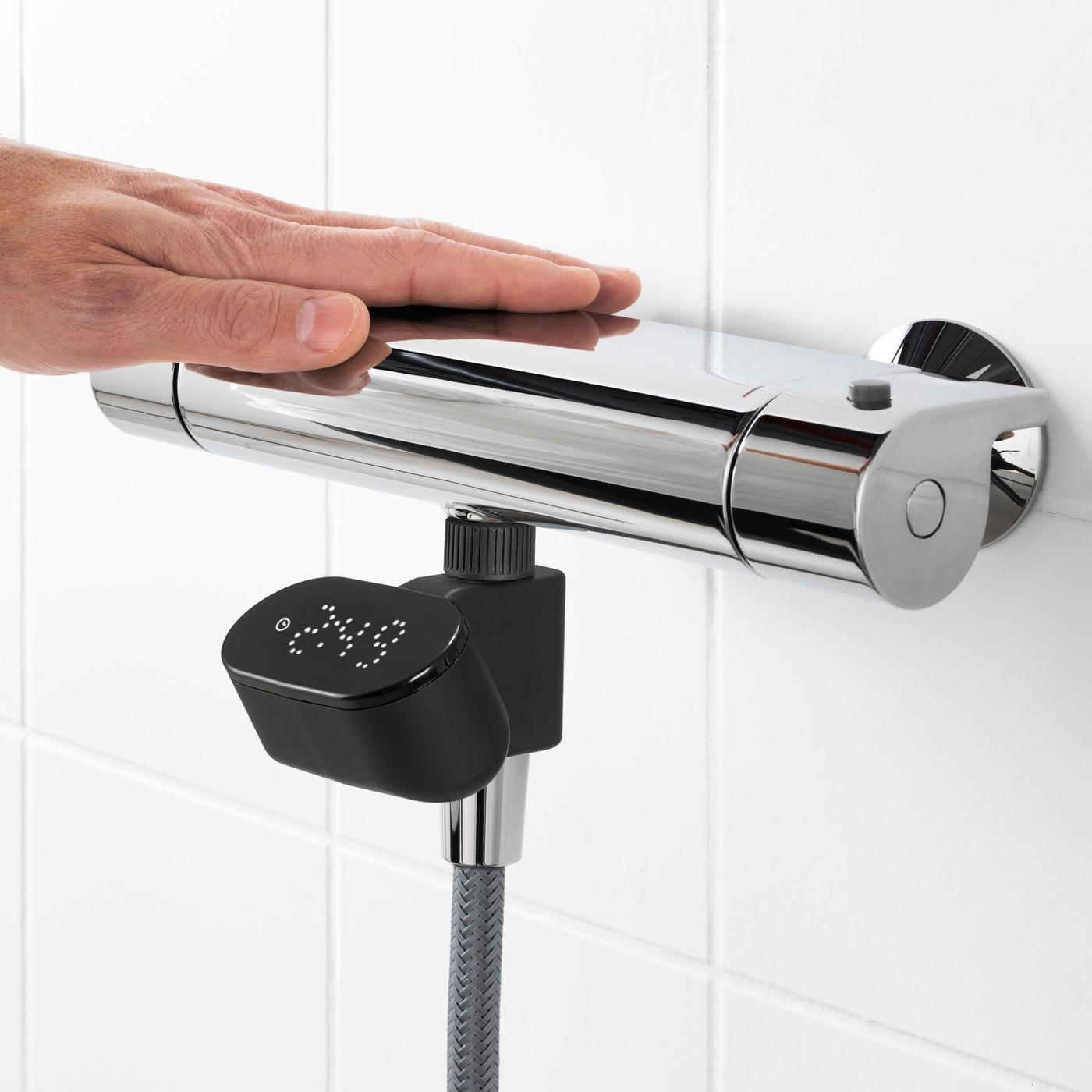 A hand resting on a shower mixer, below which is a temperature display.