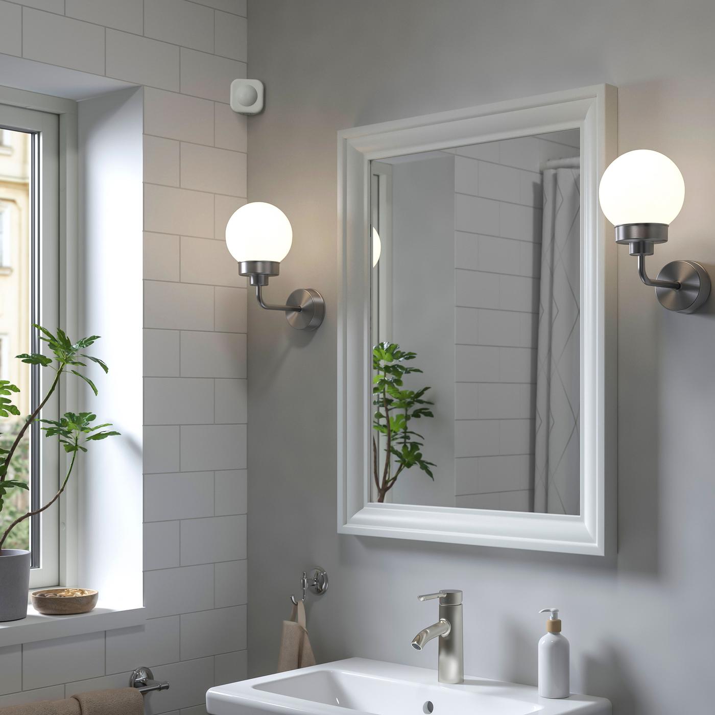 A bathroom mirror, flanked by two round wall lamps hangs over the basin. A sensor is visible on the upper wall to the left.