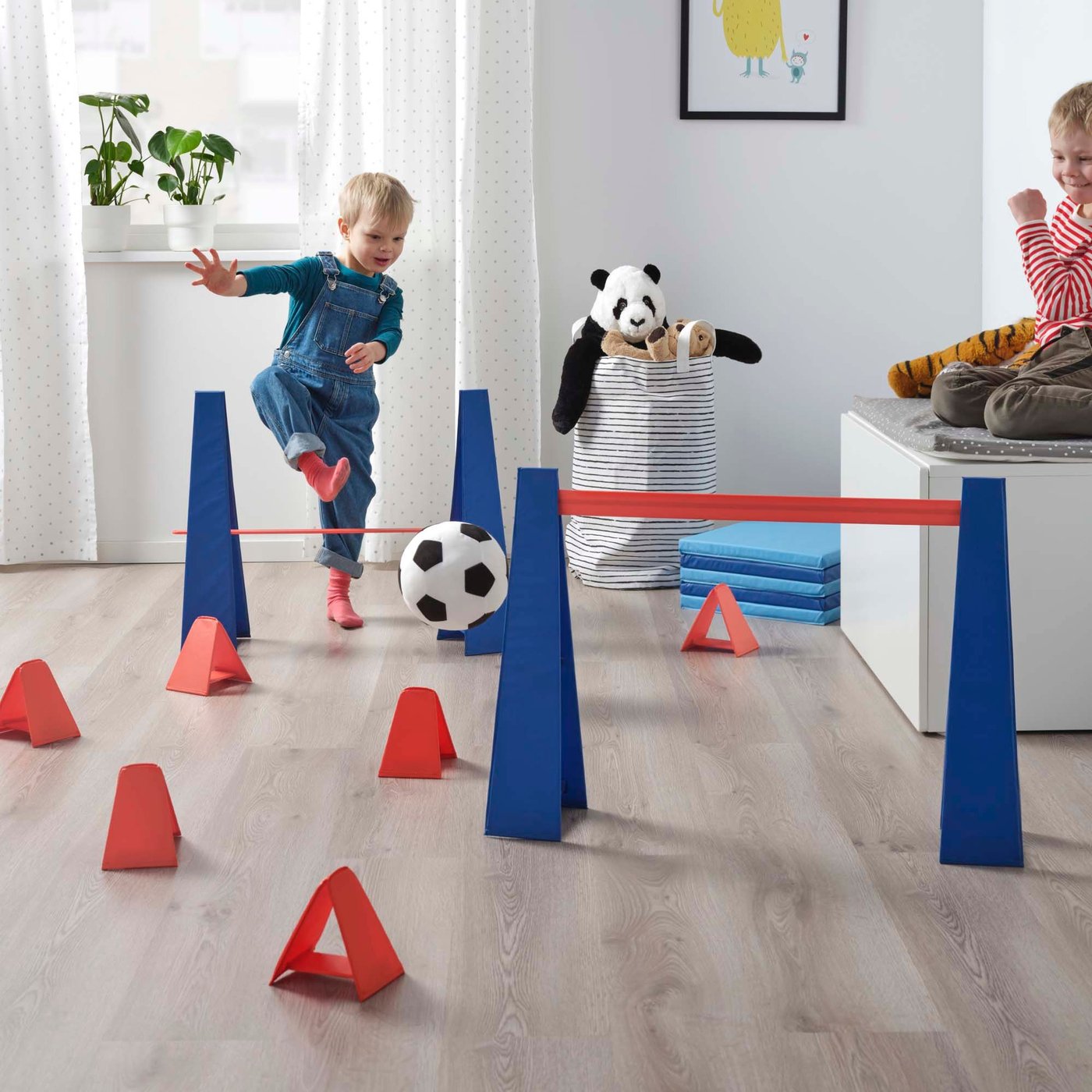 A boy playing with a football and the IKEA SKRATTMÅS obstacle in his room.