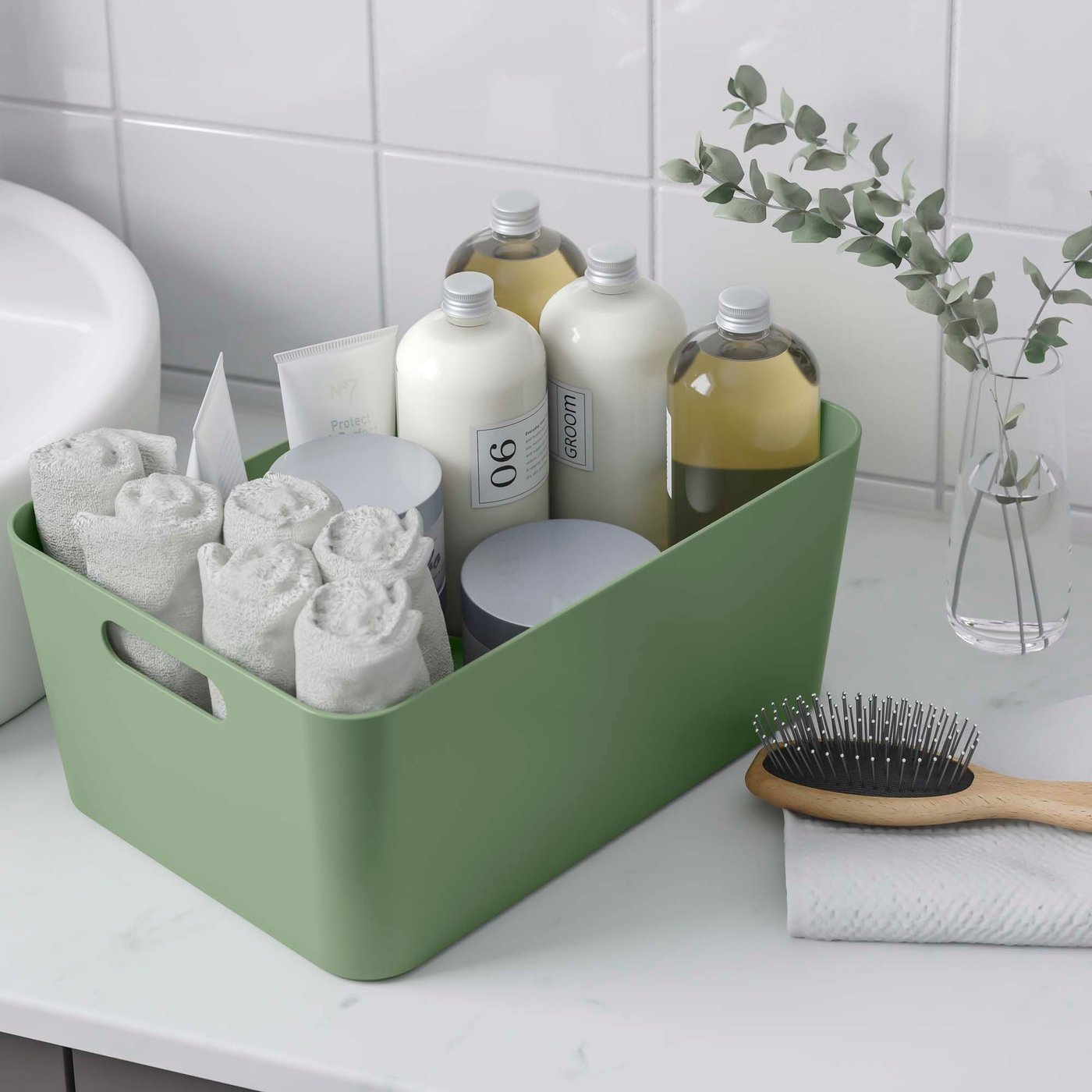 A green UPPDATERA storage container sits on a bathroom vanity unit. It is filled with soaps, shampoos and face cloths.