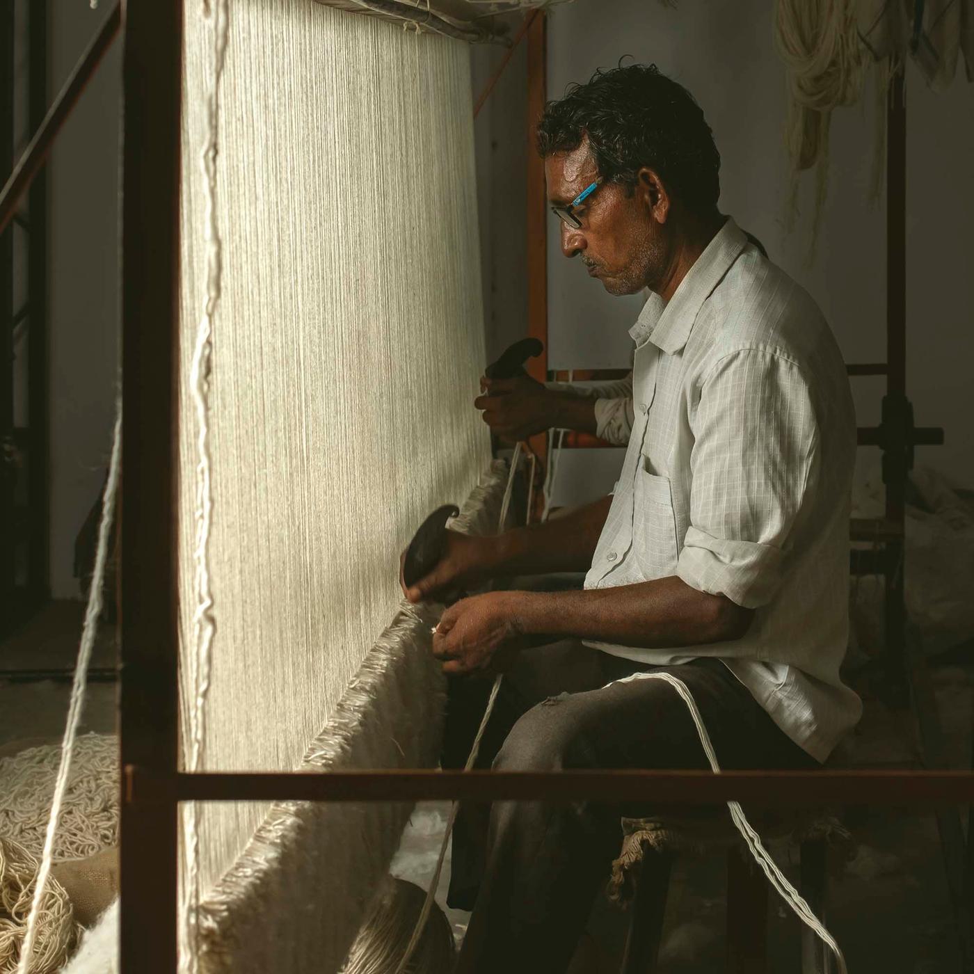 A person sits at a loom, weaving a hand woven rug.