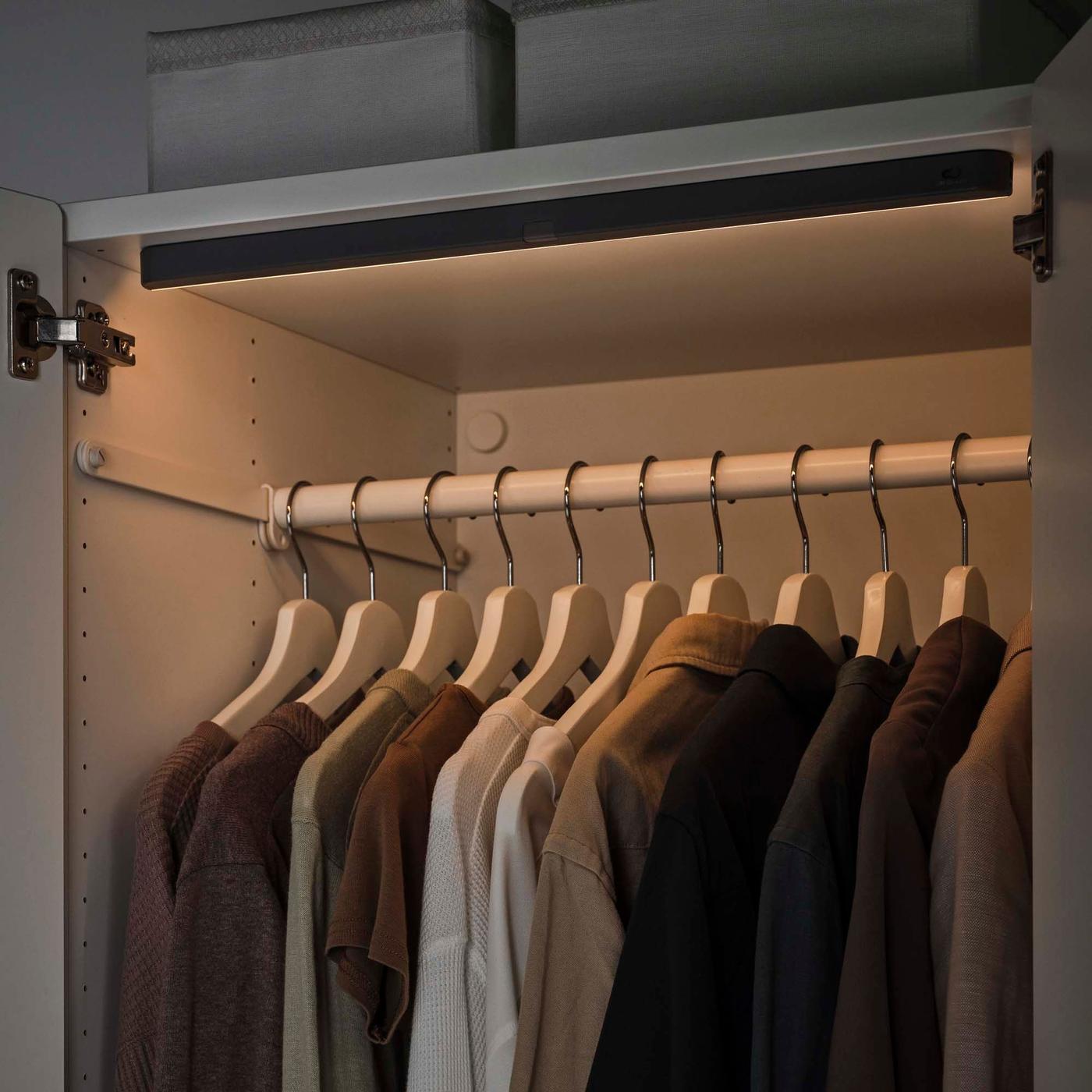 Clothes hanging in a wardrobe, illuminated by a strip light above.