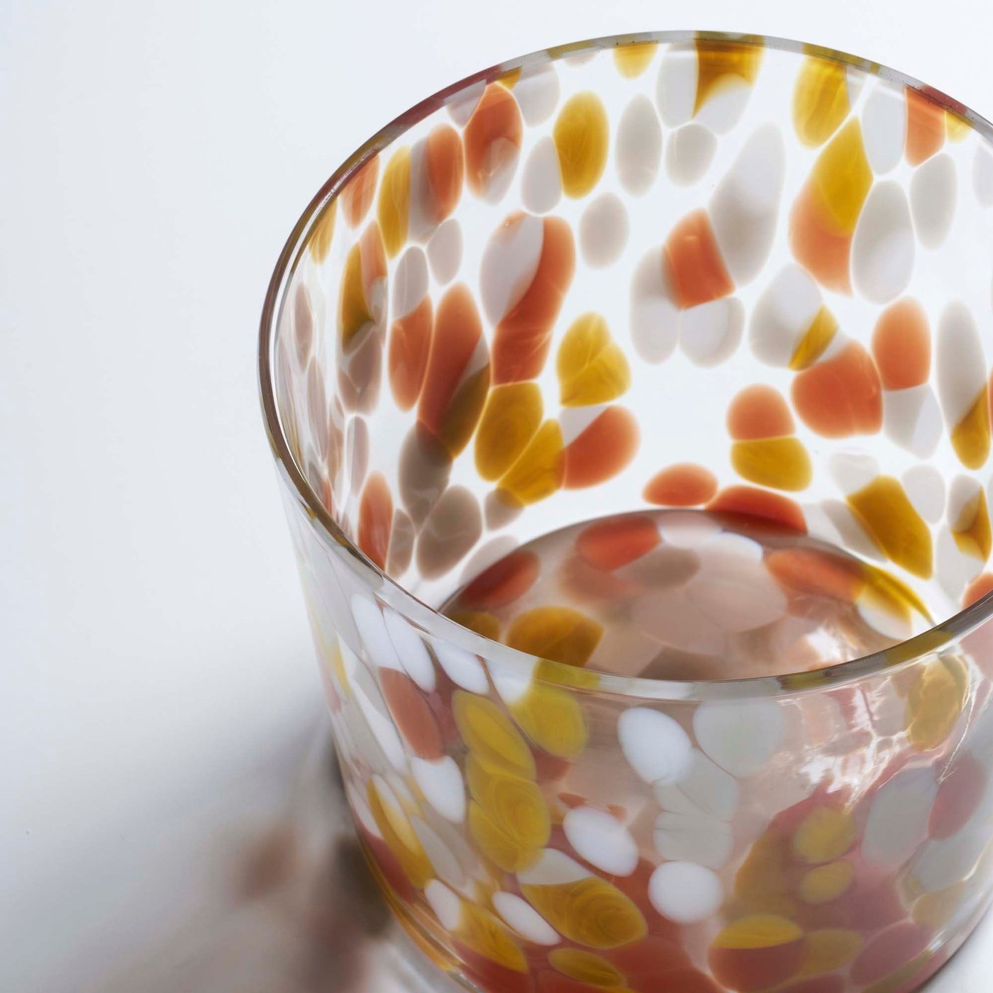 An ULLSYREN glass with a white, yellow and orange coloured spot pattern.
