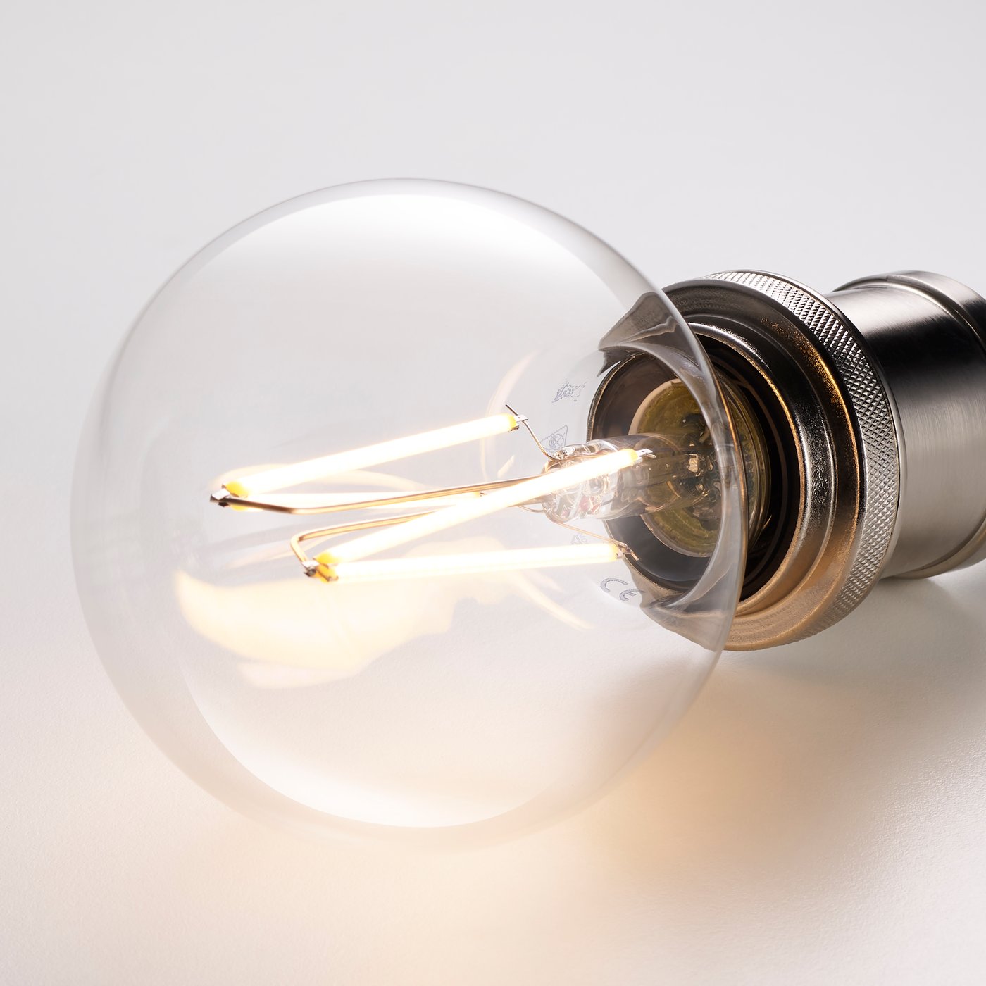 A lit filament light bulb resting on a white surface.