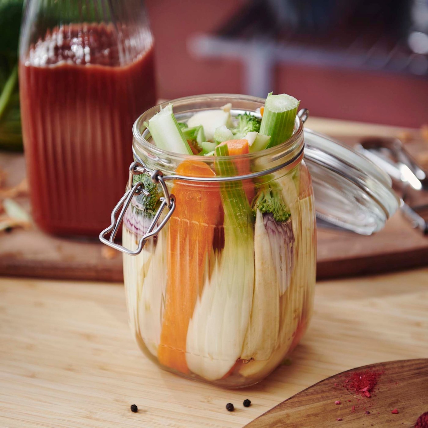 A KÖSSEBÄR pickling jar filled with vegetables sits on a table. Behind is a bottle of blended tomatoes.