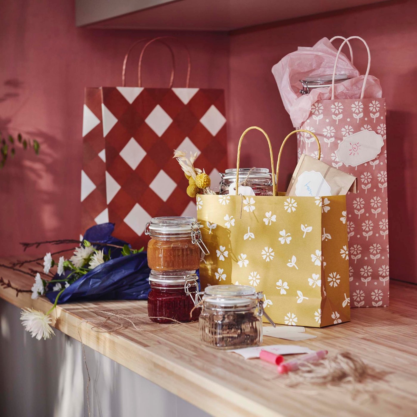 A wooden countertop filled with colourful patterned KÖSSEBÄR gift bags and jars filled with jams and dried food.