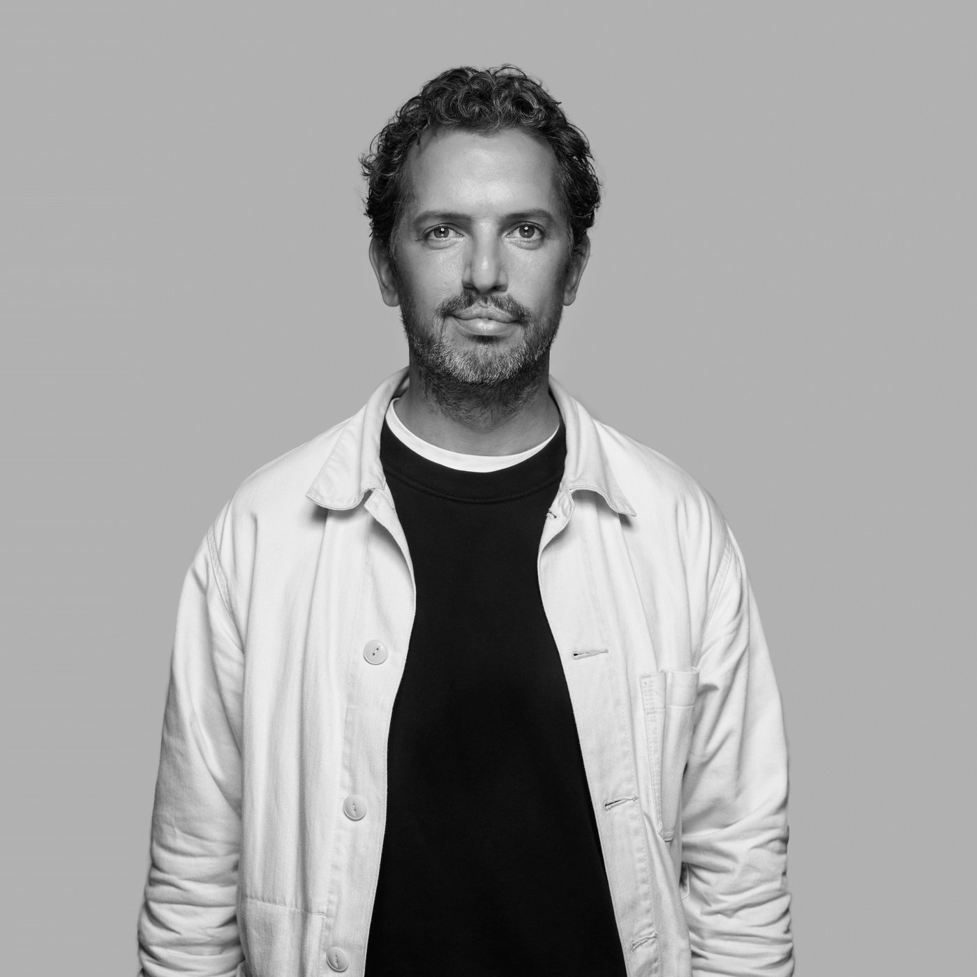 Black-and-white portrait of designer Lex Pott wearing a light jacket over a dark shirt, standing against a plain background.