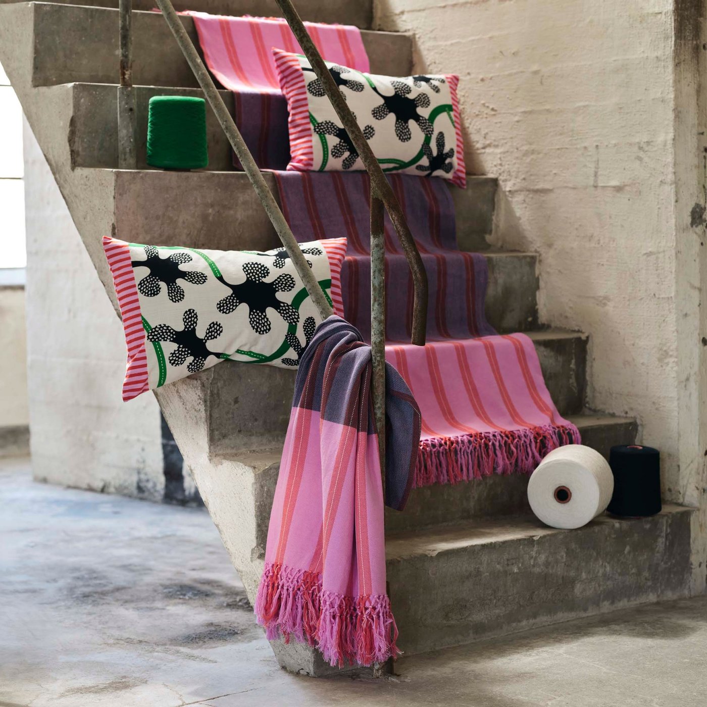 Woven throws and printed cushions are laid out on concrete steps.