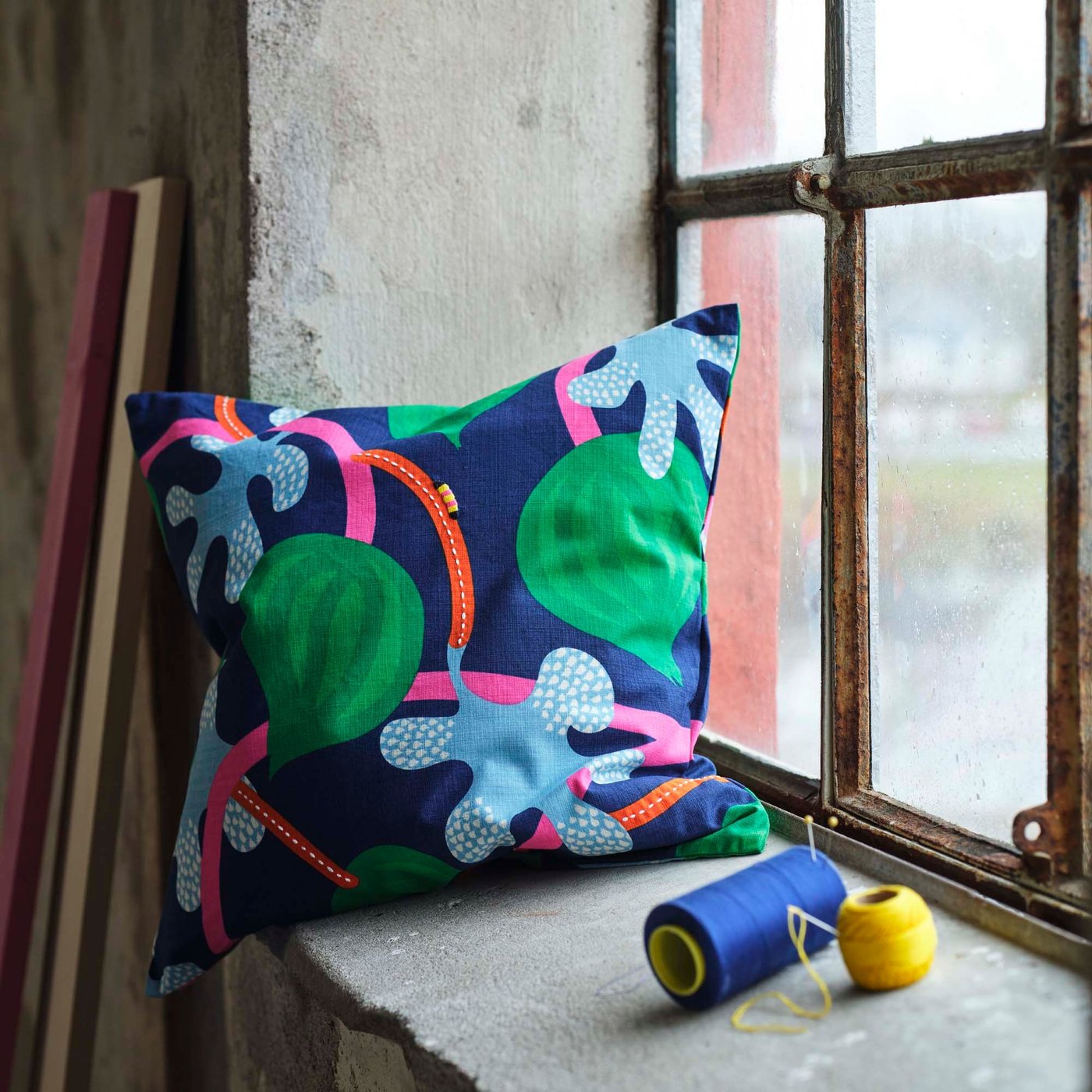 A brightly coloured printed cushion on a window ledge next to a window.