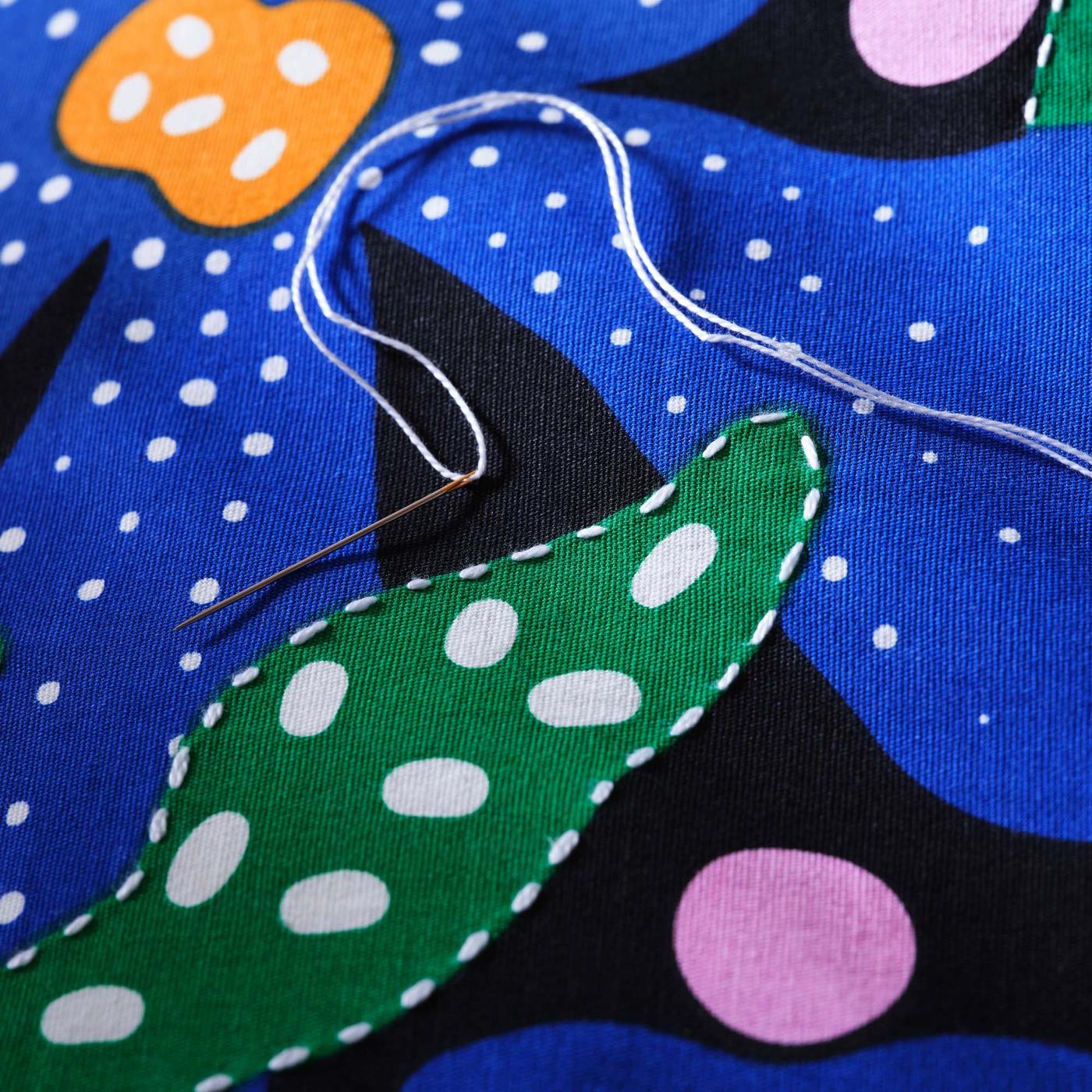 A close-up of a colourful cushion cover, with hand stitched details.