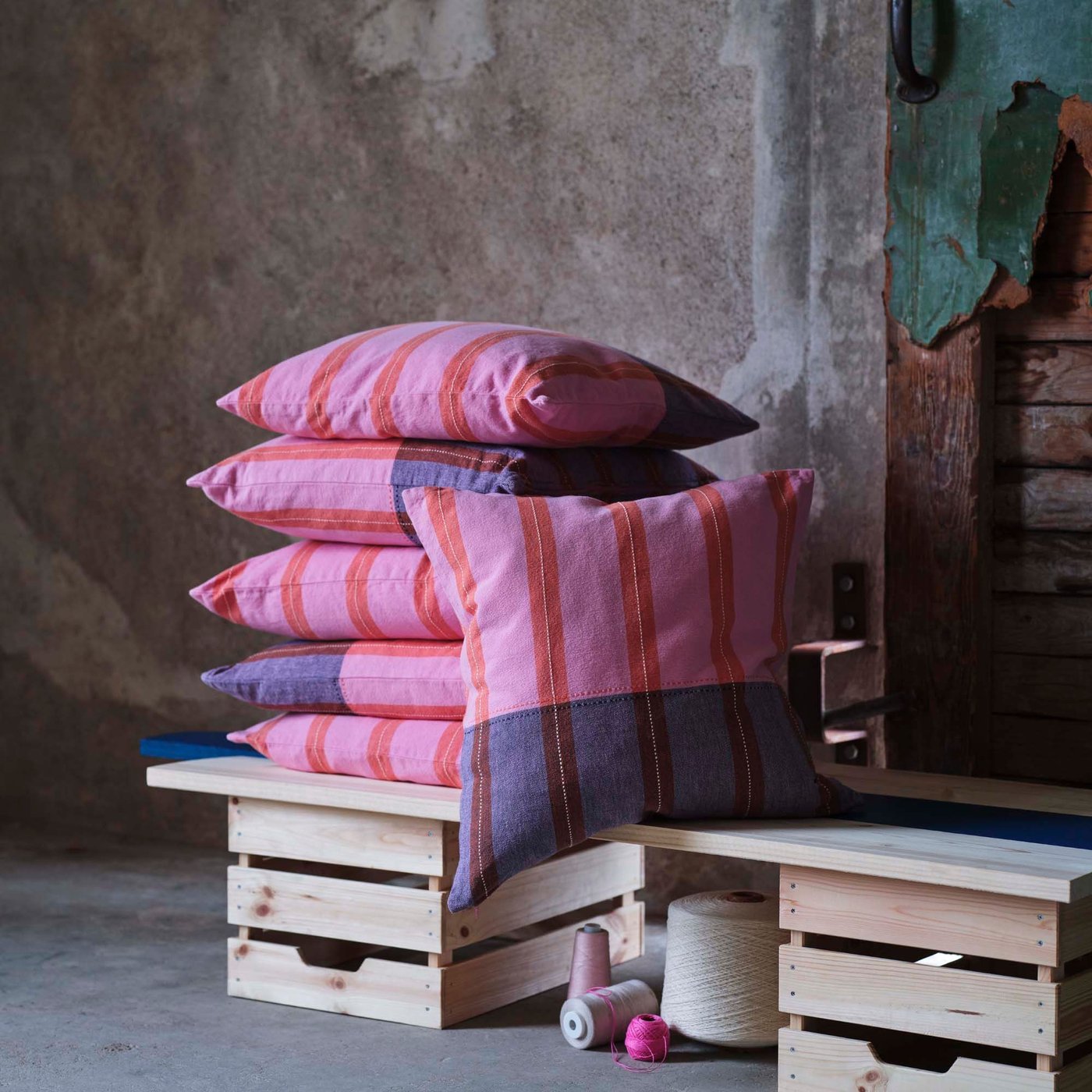Pink and blue cushions stacked on a stool against an industrial background.