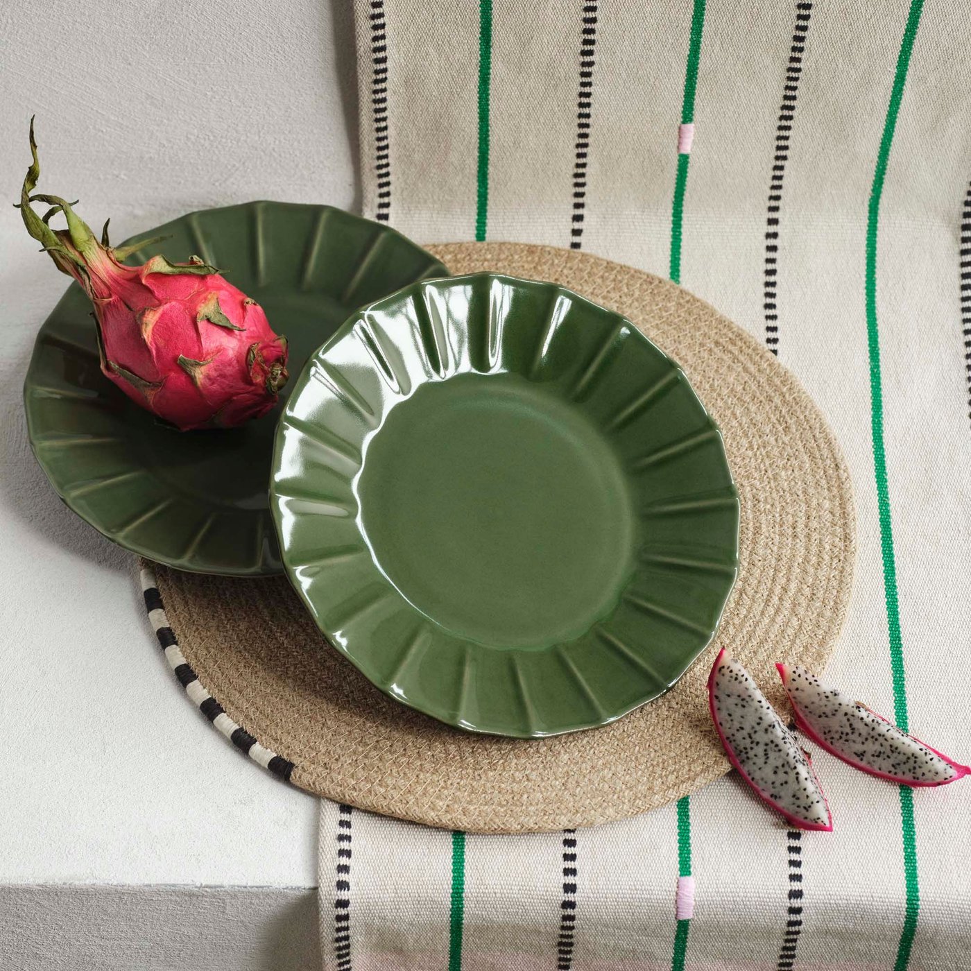 Two green plates and a dragon fruit on a striped table runner.