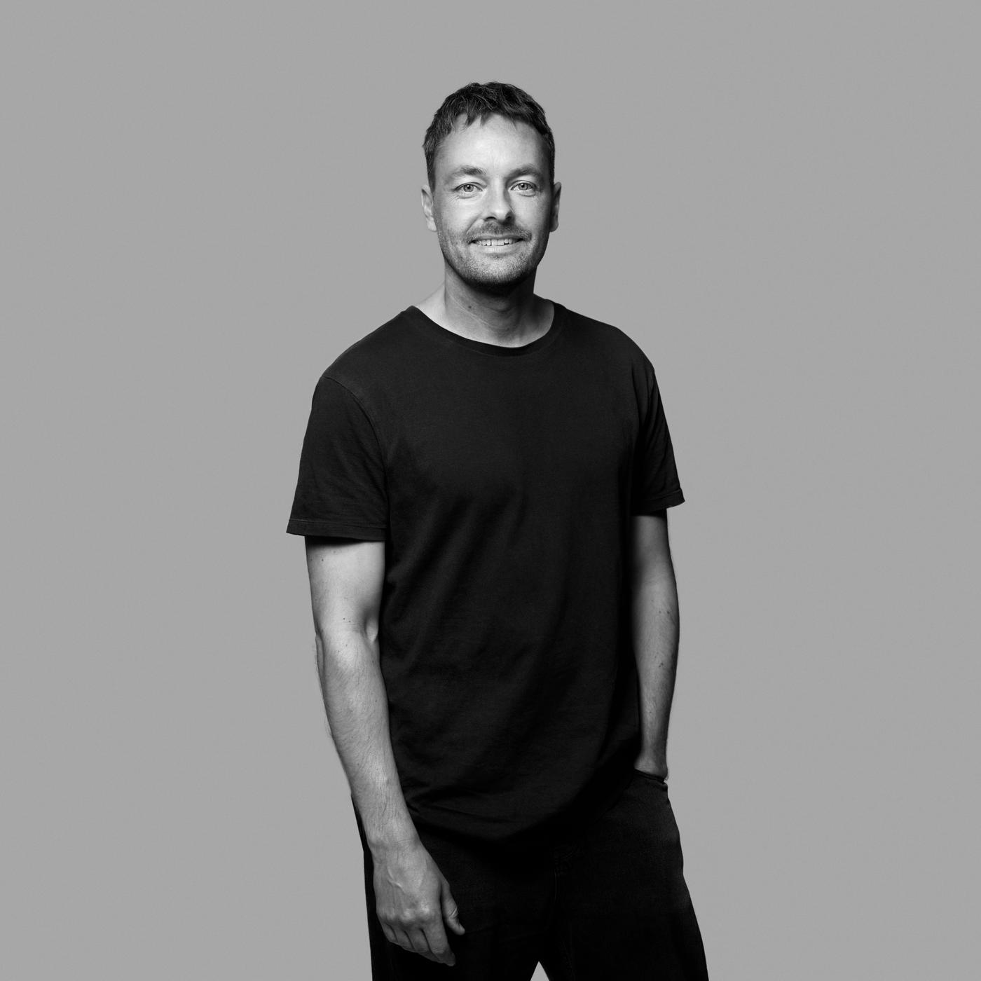 A black and white portrait of designer Mikael Axelsson standing and smiling.