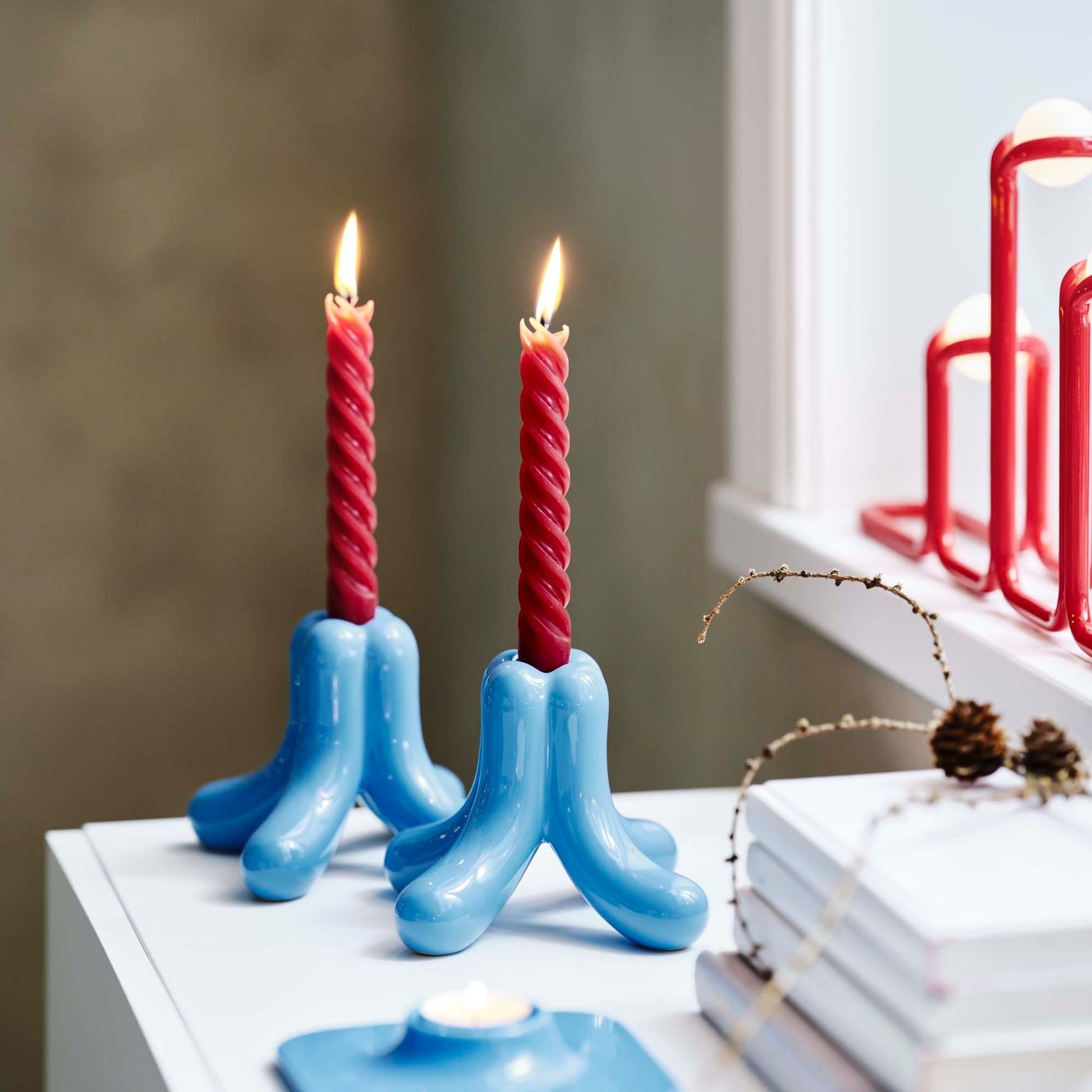 Red taper candles side by side in sky blue holders, each with four rounded feet.