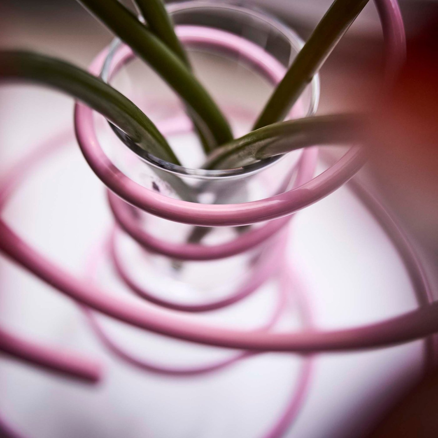 Close-up of a pink spiral-shaped steel vase seen from above, showing stems of flowers inside.