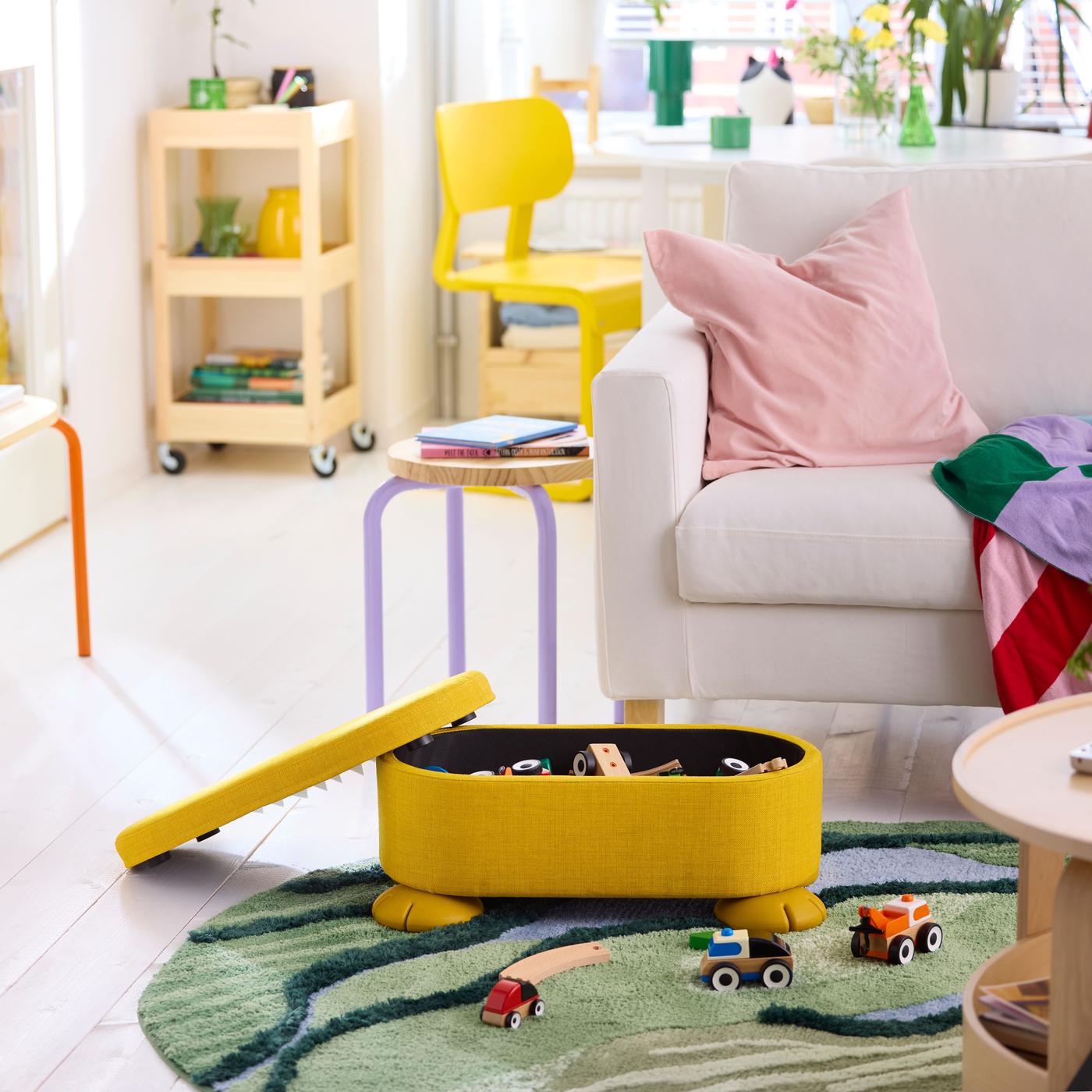 A yellow round pouffe with storage, partially open and filled with toys, placed in a home furnishing background.