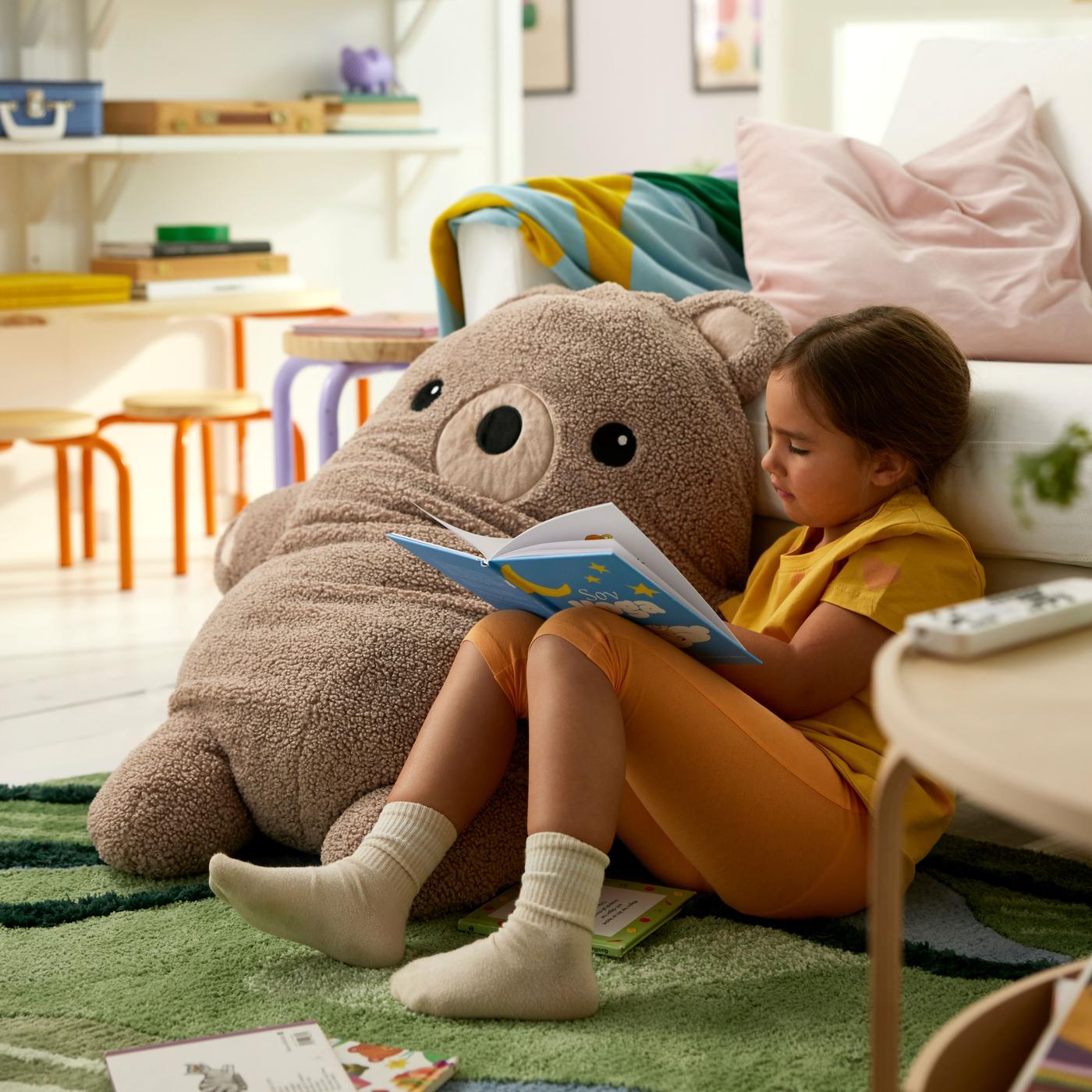 A young child relaxing and reading beside a soft toy bear in a cozy indoor setting.