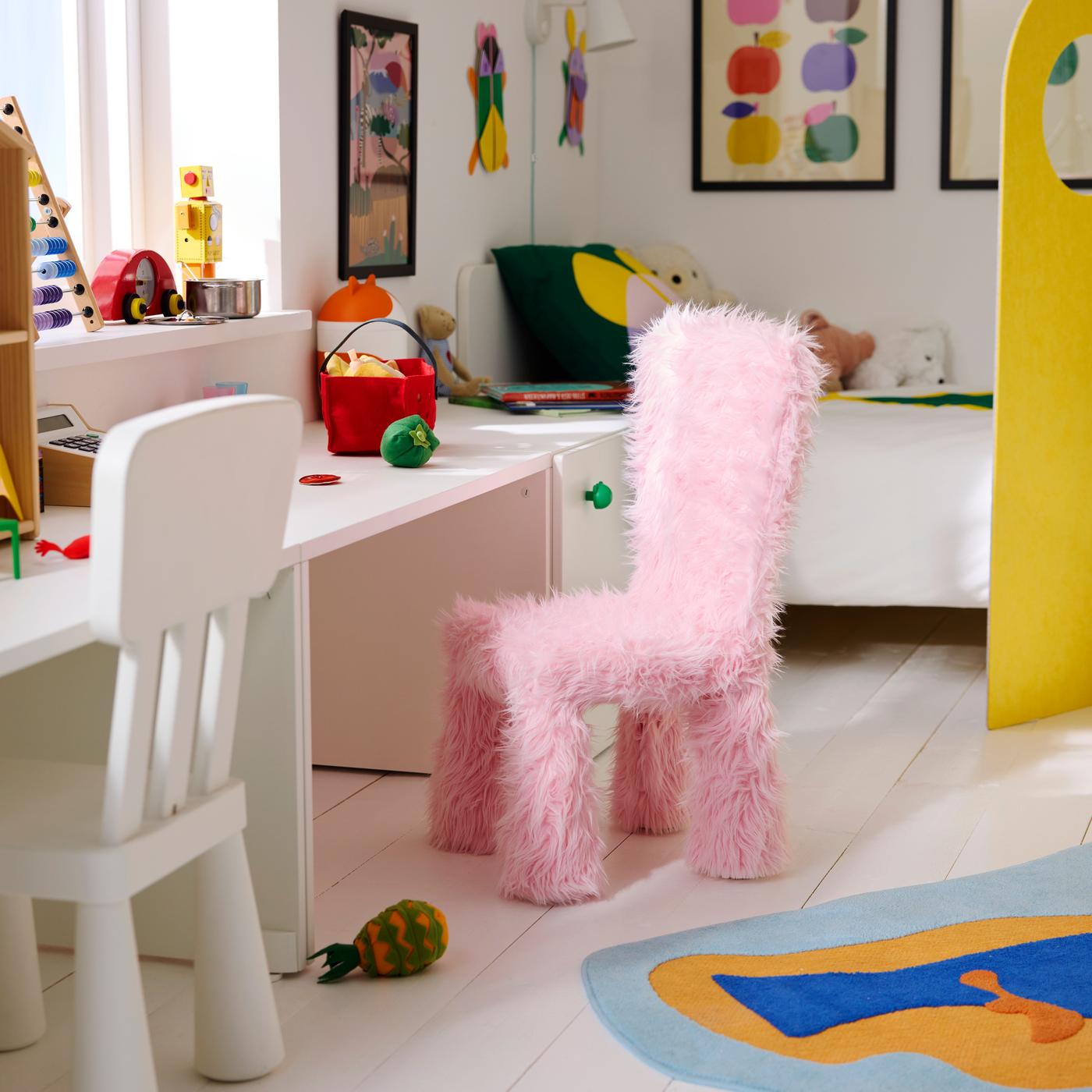 A pink furry chair placed in a children’s room with a small table and colorful decor.