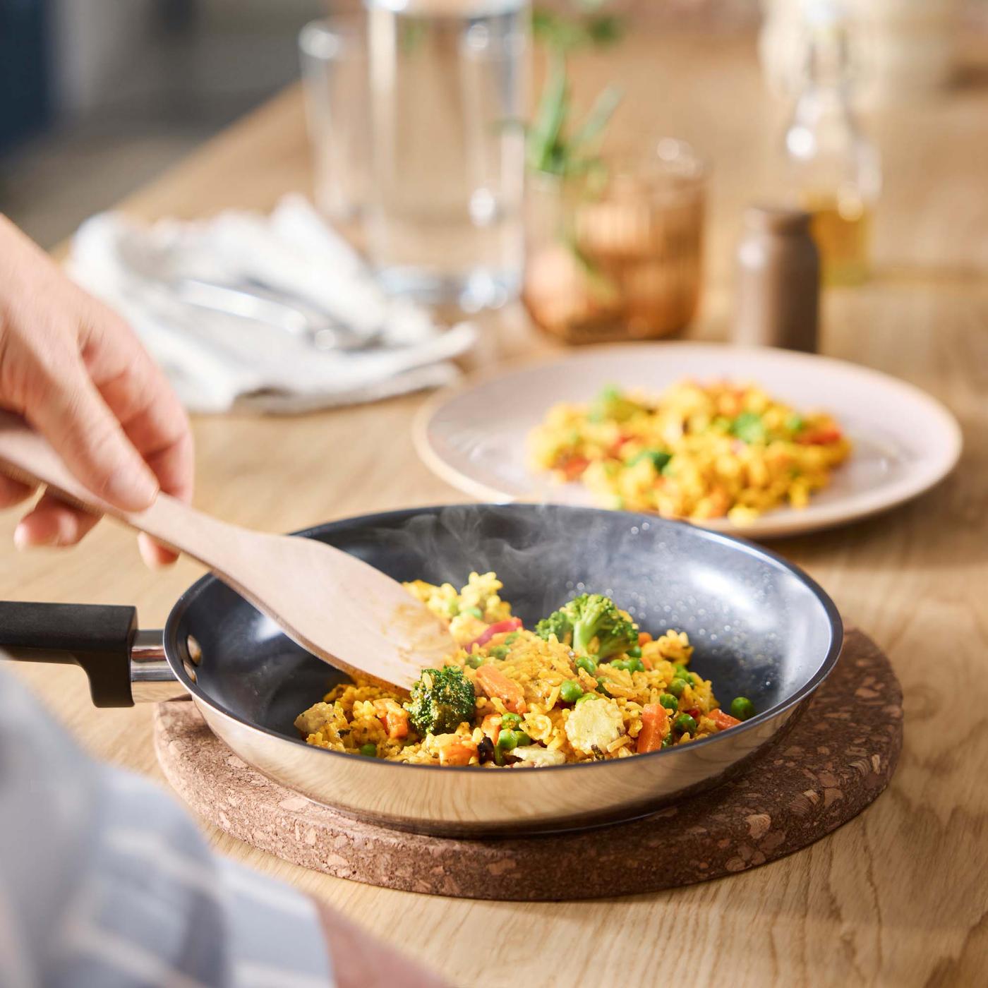 A close-up of a person serving up LÄTTLAGAT rice mix with vegetables in a pan, with a wooden spatula.