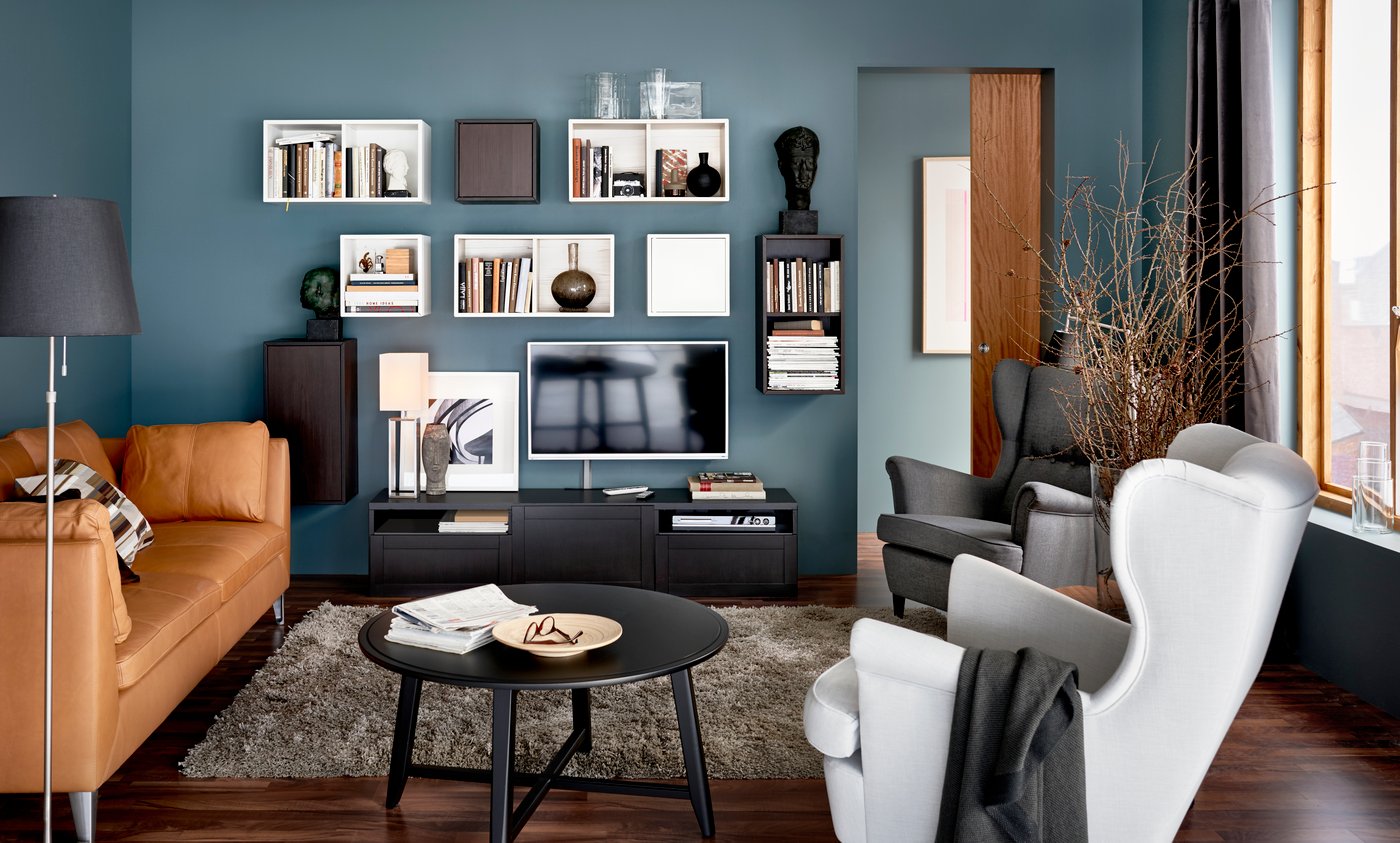  A blue living room from the 2016 IKEA catalogue, with storage and a wall-hung TV on the wall. In the foreground is a natural leather sofa and some armchairs.