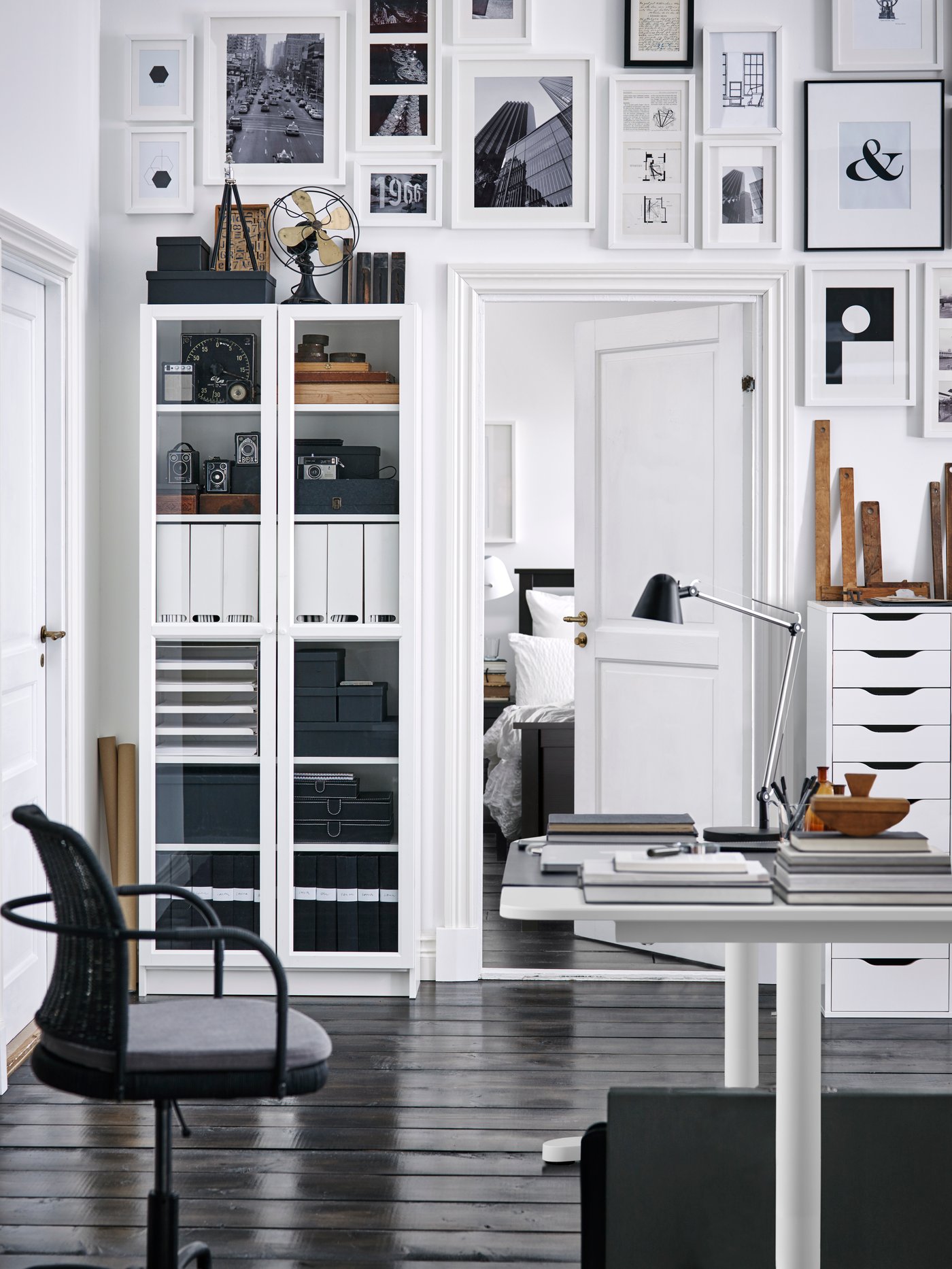 The wall of a home office area with a white BILLY bookshelf and lots of images on the wall above an open doorway, from the 2016 IKEA catalogue.