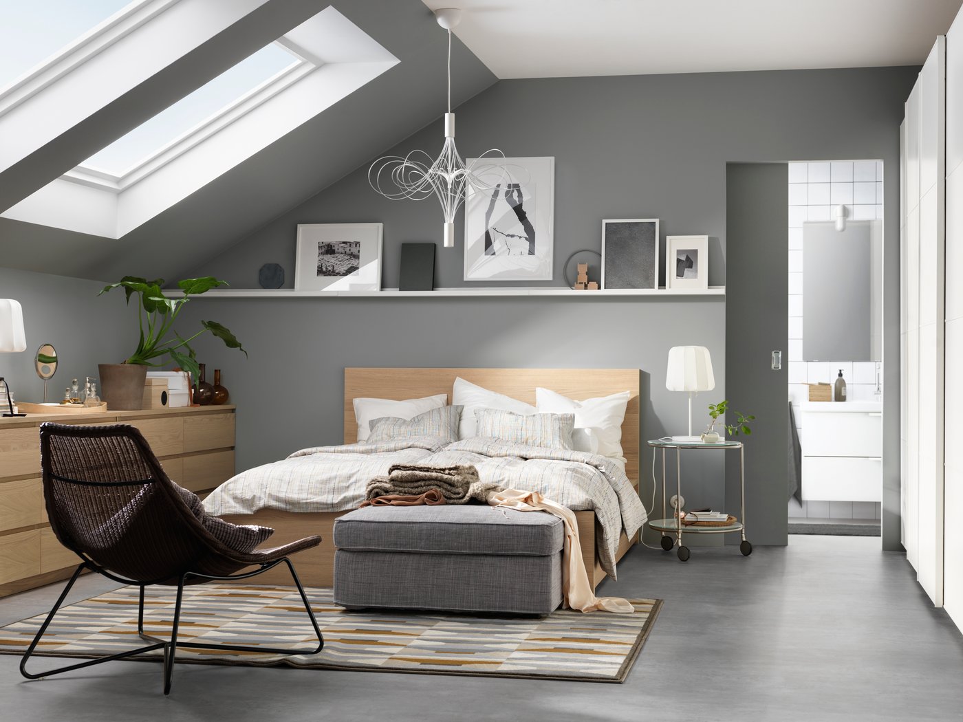 A grey bedroom with a sloping ceiling and a shelf above the bed featuring framed images.