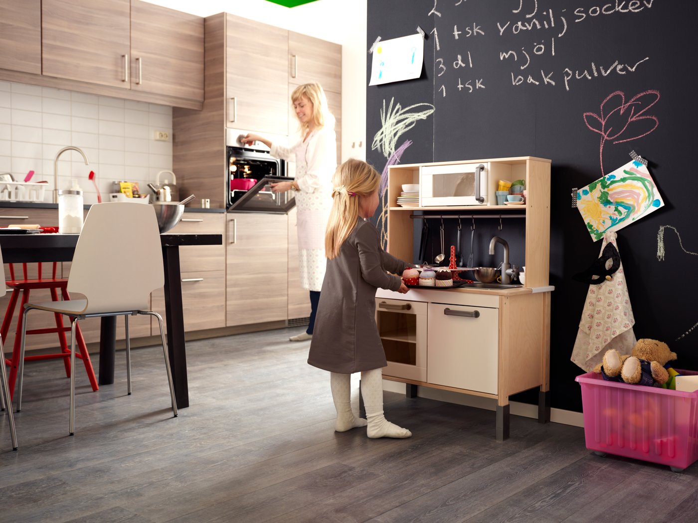 A young child plays with children's kitchen, with a chalkboard with scribbles on the wall behind it.