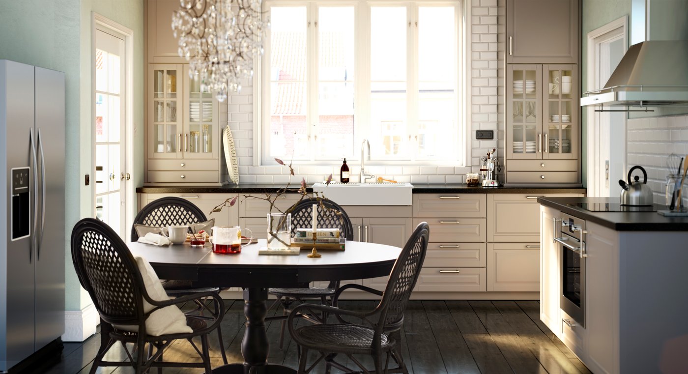 A pale kitchen with a dark wood round dining set, with a glass chandelier hanging above.