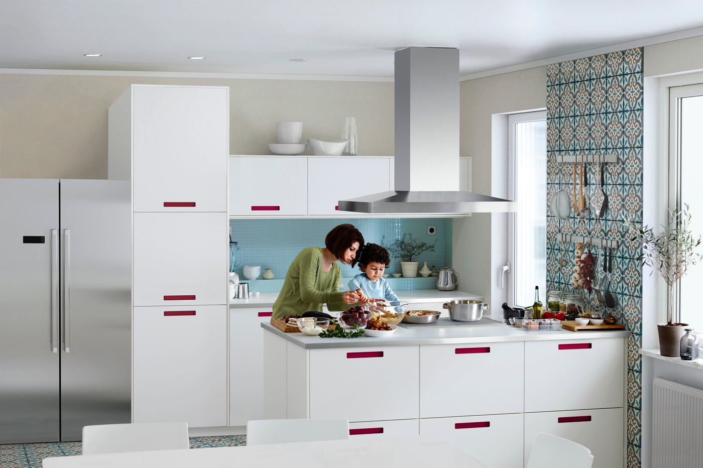 Three people stand in a turquoise tiled kitchen with white kitchen units. They are cooking and baking.