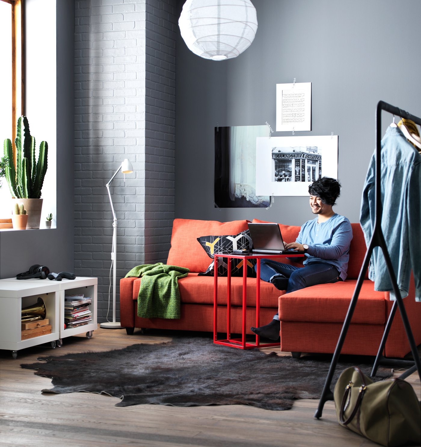 A person in a grey living room sits on a red sofa, working at a red table.