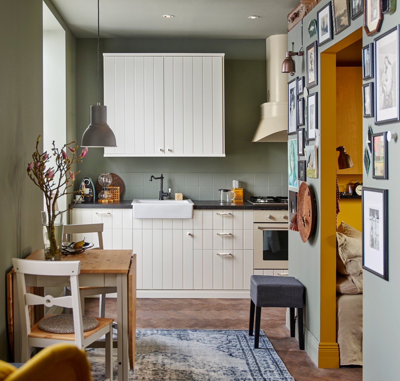 A sage green kitchen with traditional style white wood kitchen doors and a rustic style sink.