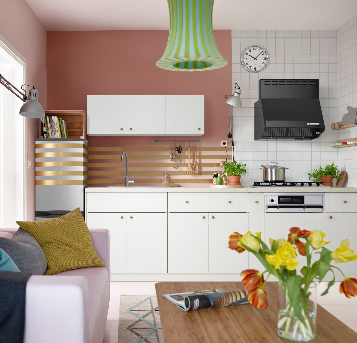 A pink kitchen and living room area. In the kitchen, the wall and refrigerator are adorned with gold horizontal stripes.