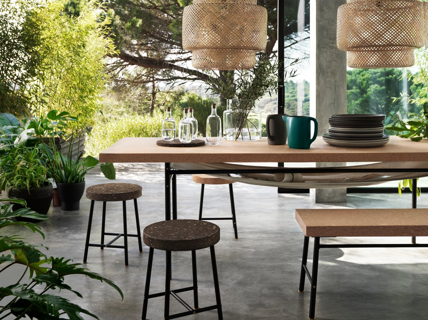 An open indoor-outdoor area with cork tables and chairs and rattan lampshades, all from the SINNERLIG collection.