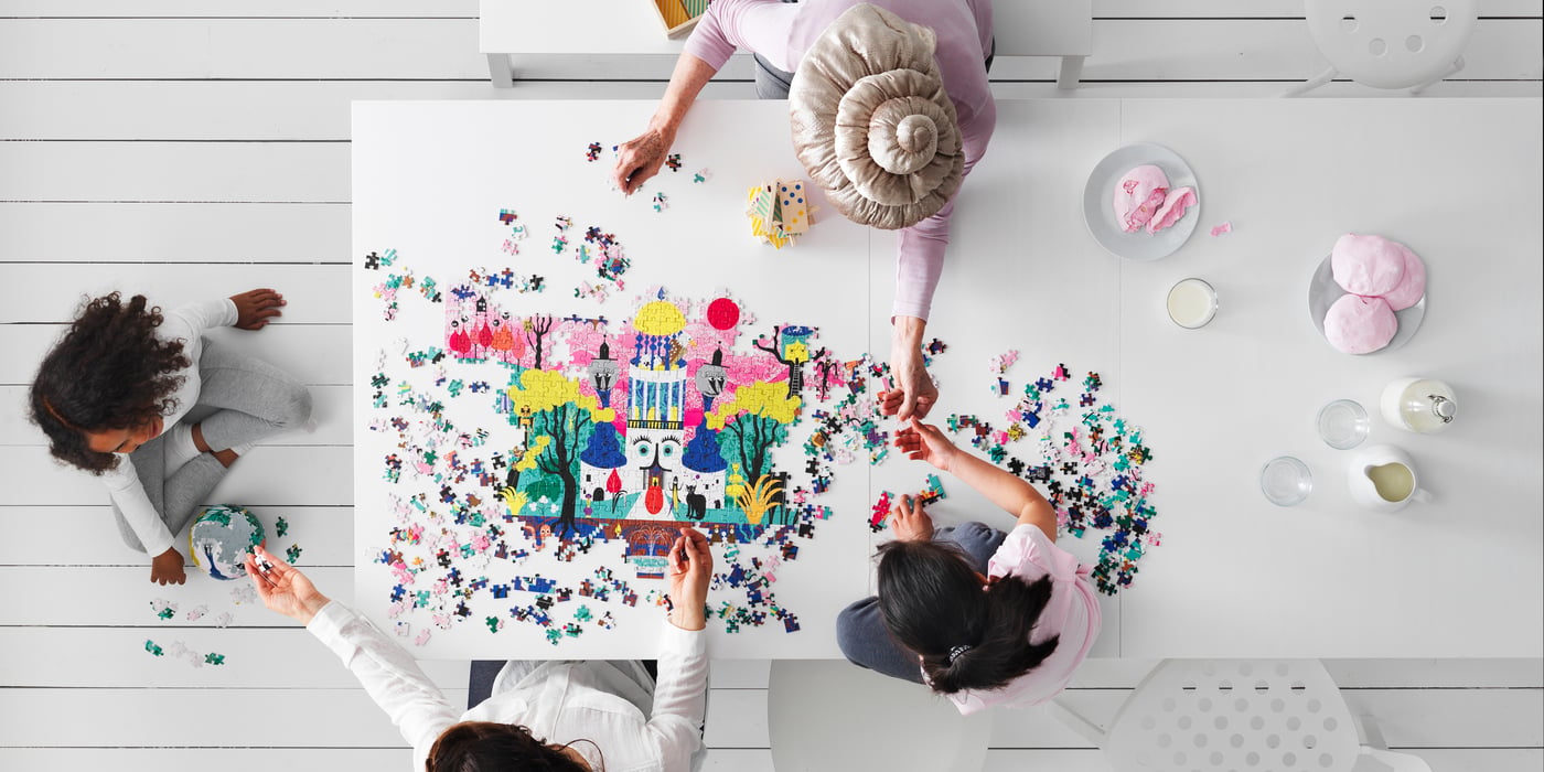 Overhead view of a group of people assembling a colourful jigsaw puzzle on a white table.
