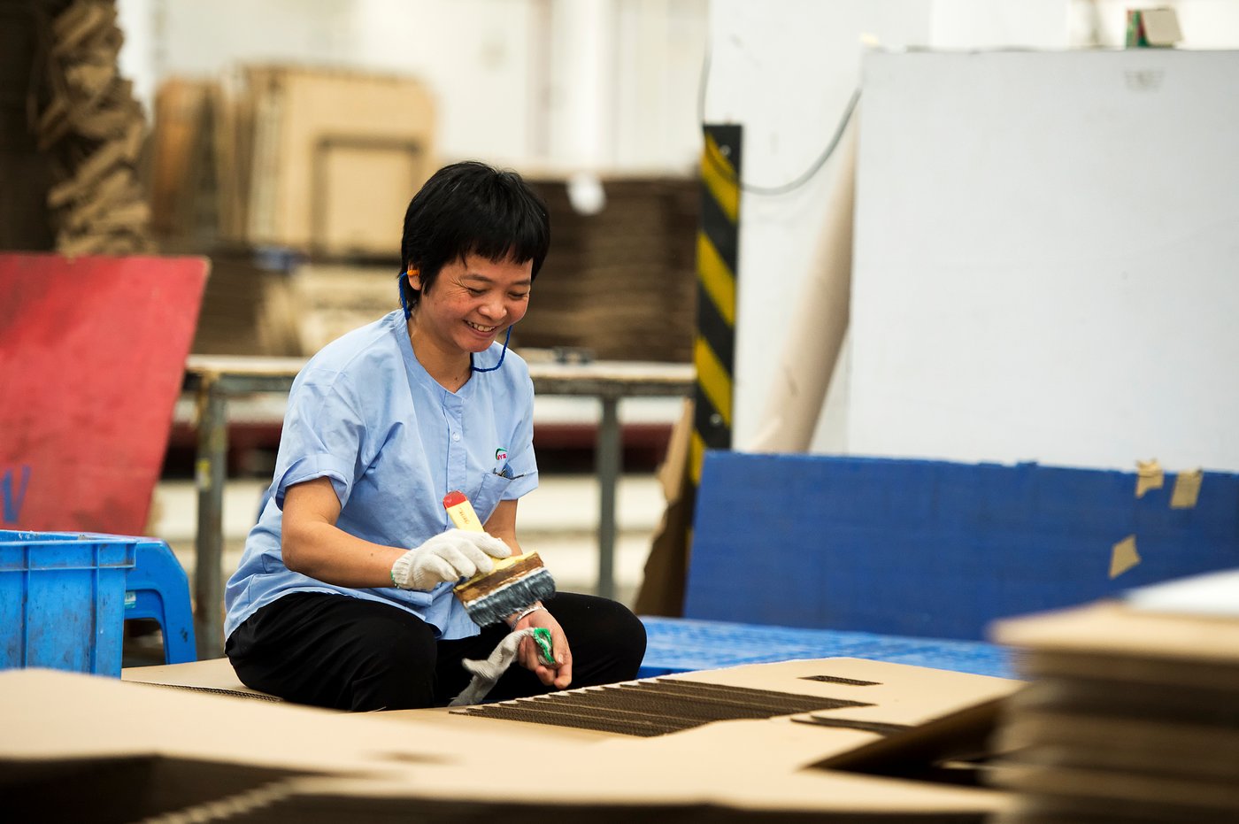A person in a factory setting, painting while sitting on the floor.
