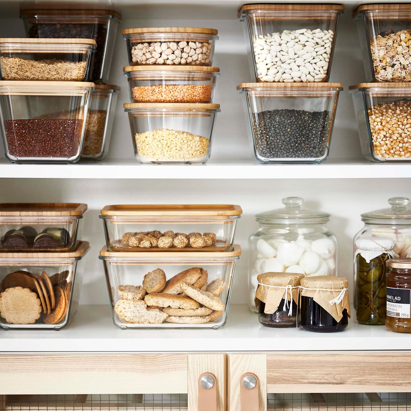 White shelves laden with stacks of glass jars with a bamboo lid containing various dry foods.