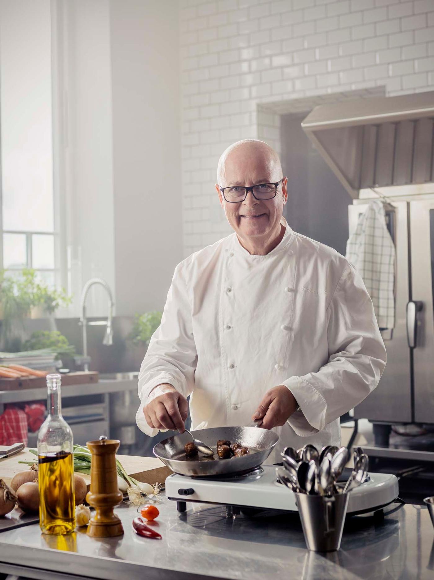 Chef Severin Sjöstedt stands in a kitchen. He smiles at the camera as he cooks meatballs.