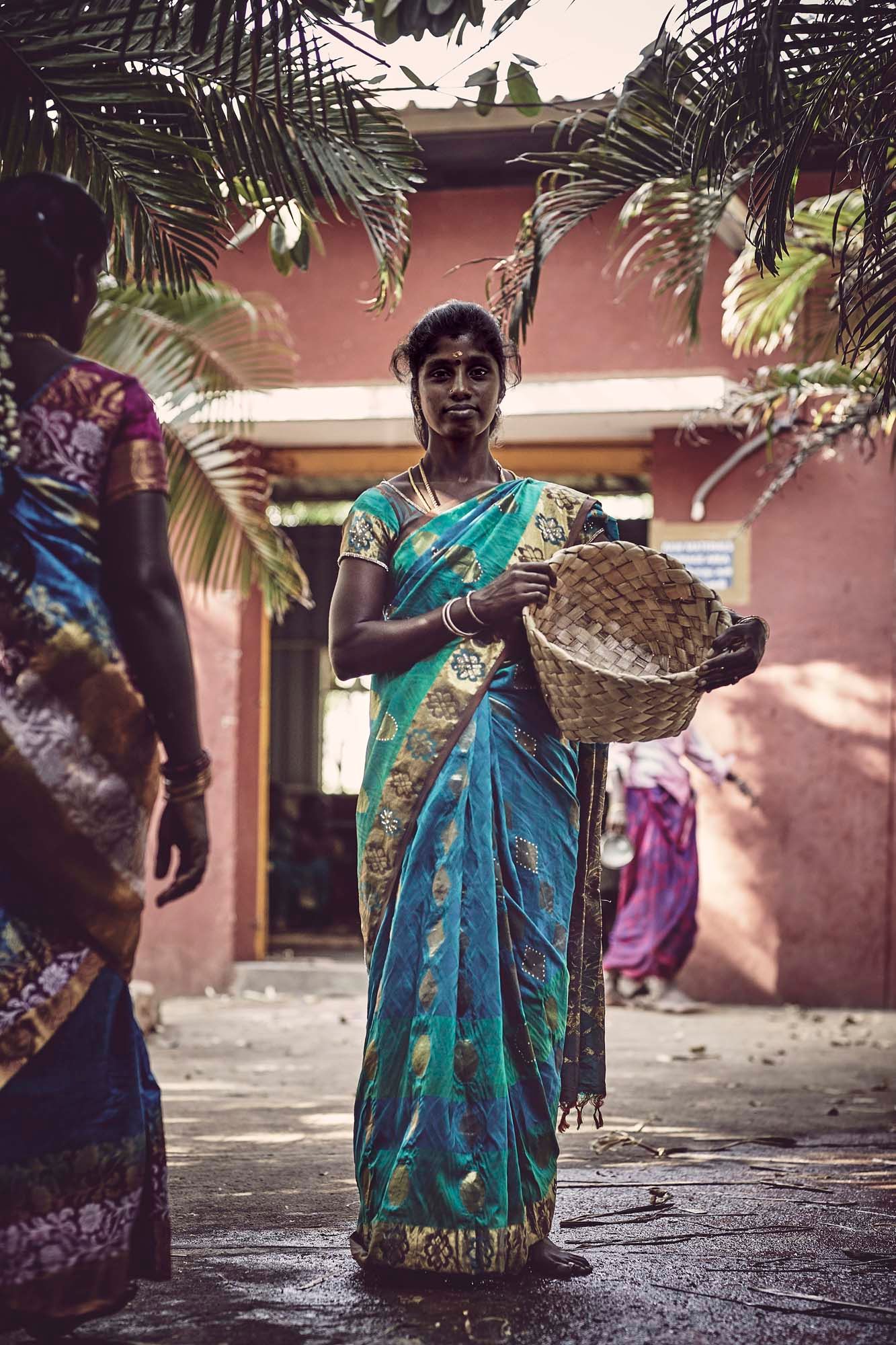 A woman stands outside. She is holding a basket.