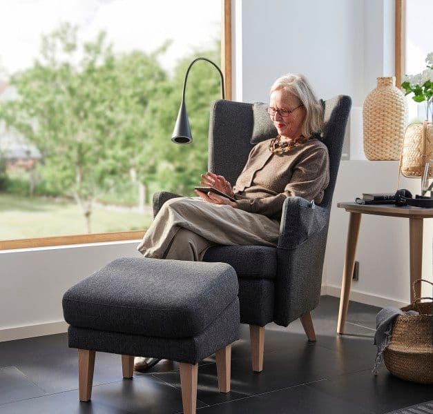 Woman sitting in OMTÄNKSAM armchair with footstool
