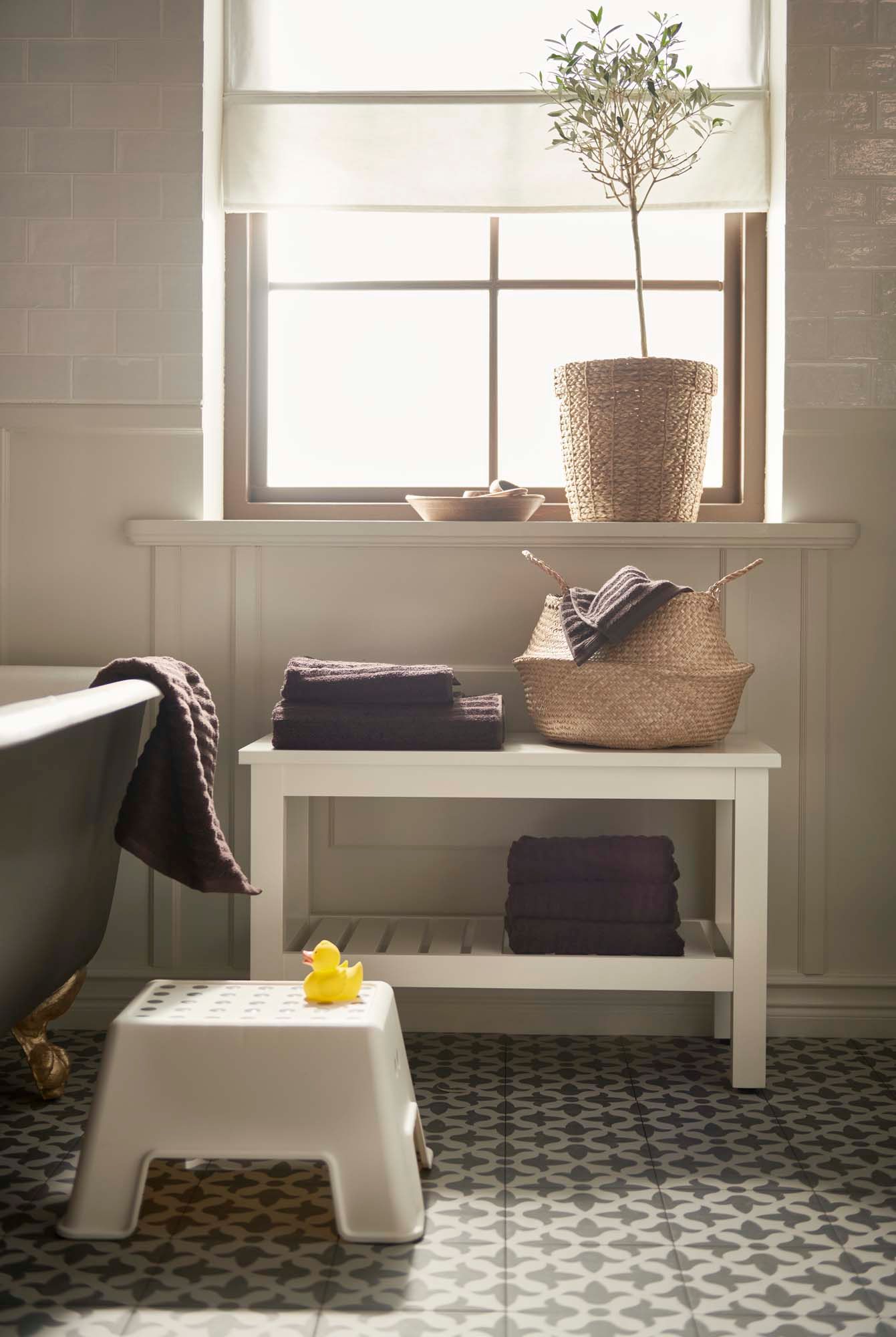 A bathroom with a bath. In the window is a plant. Below are towels.