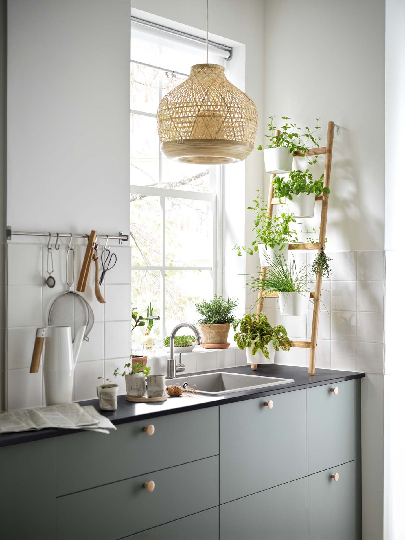The sink area of a green SEKTION kitchen, with a bamboo plant stand leaning against the wall in front of the window.