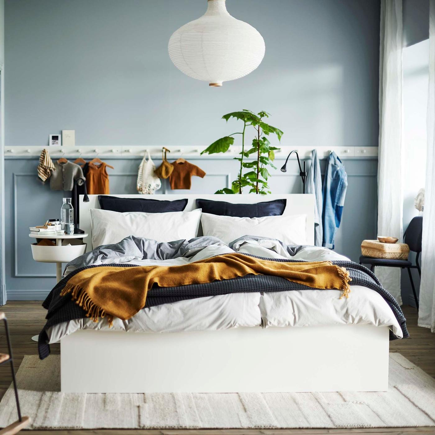 A double bed with duvets and blankets in a bedroom. Behind is a row of hooks where baby clothes hang.
